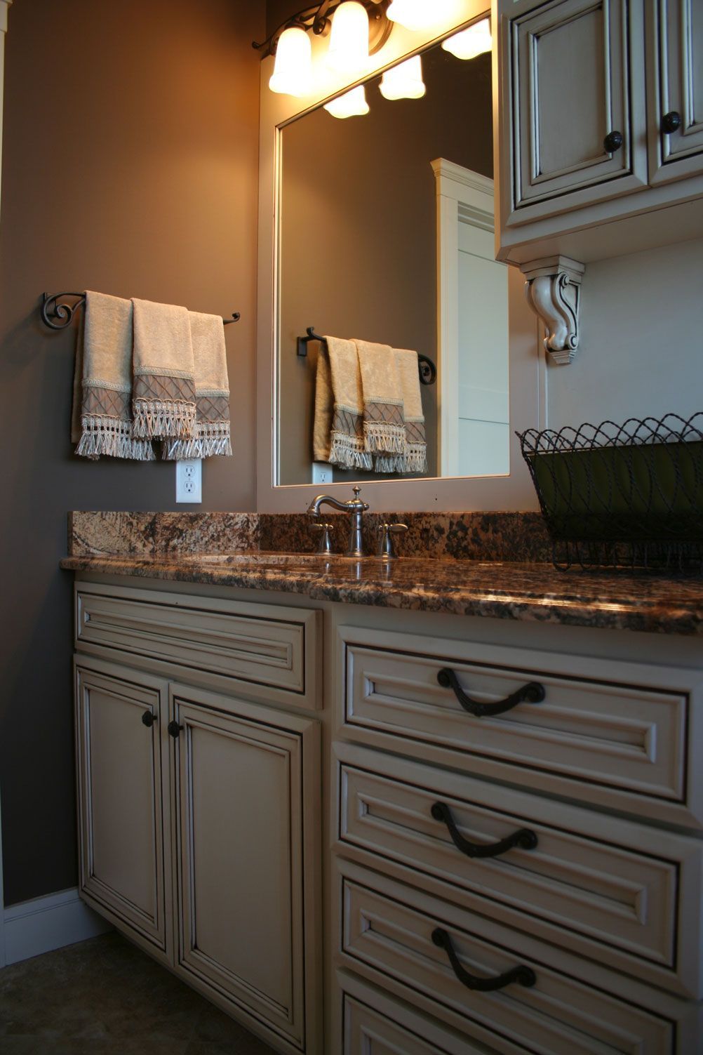 Bathroom with cream-colored vanity, brown countertop, towels on a rack, and a mirror above the sink.