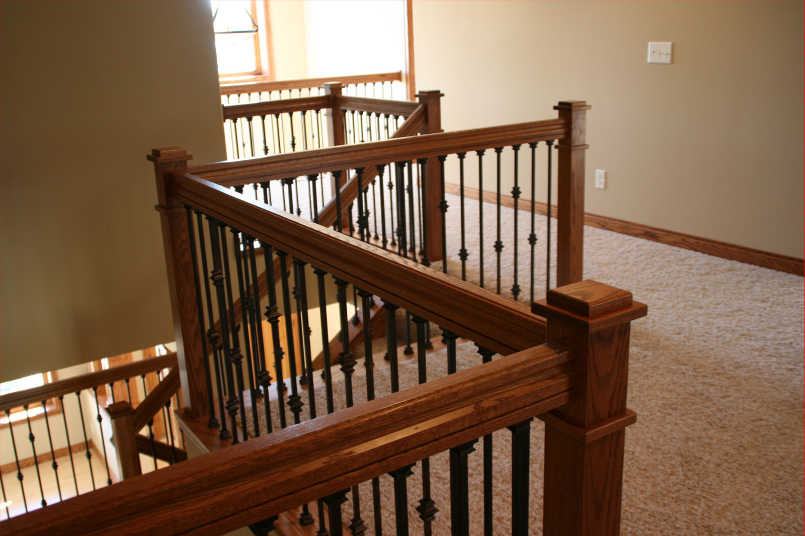 Wooden staircase with dark metal spindles and carpeted landing, beige walls.