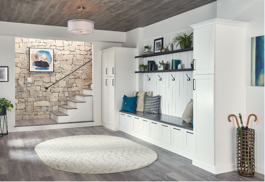 Entryway with white built-in storage, bench, and hooks. Stone staircase leads up; circular rug on gray floor.