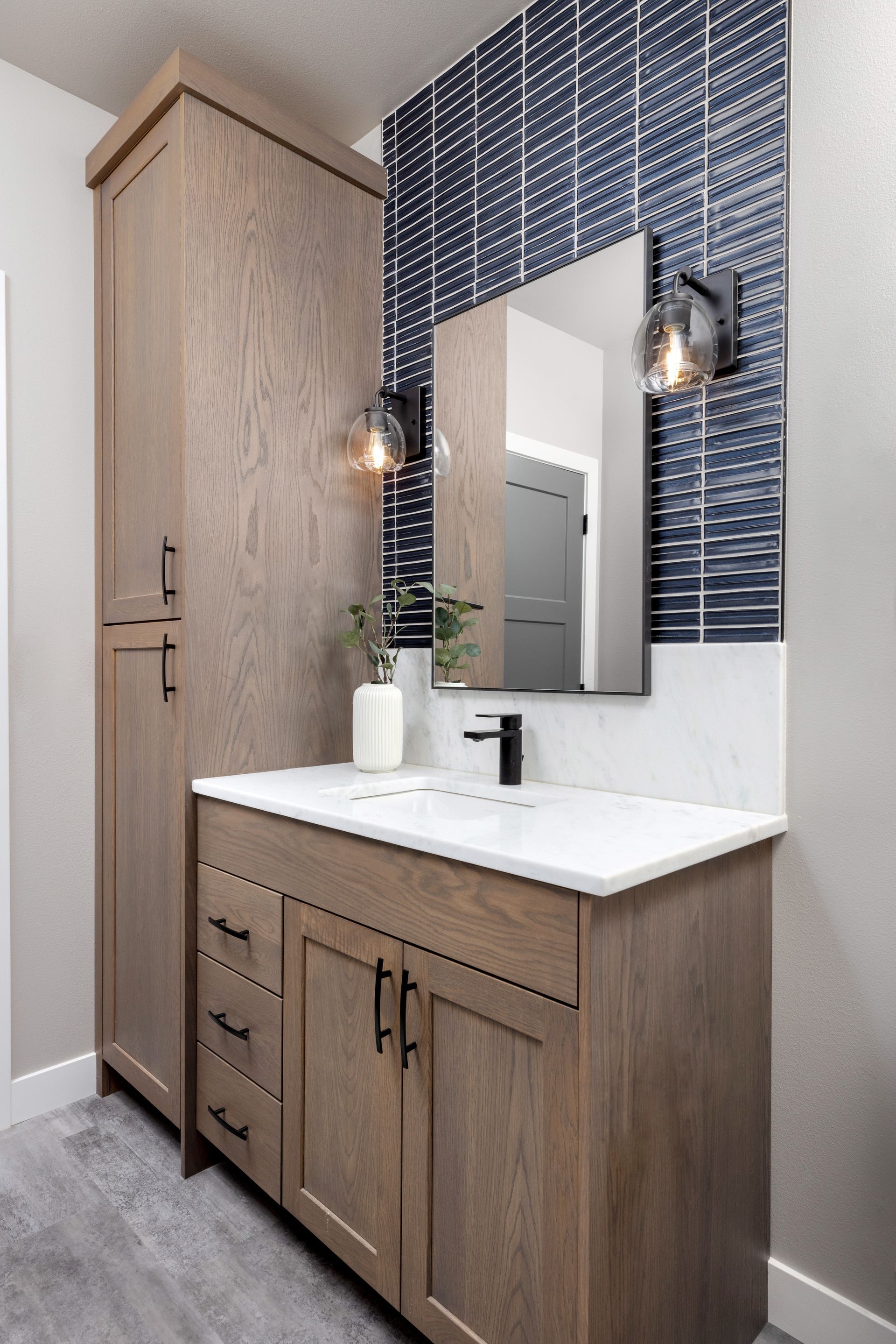 Bathroom vanity with blue tile backsplash, wooden cabinetry, and a tall storage cabinet.