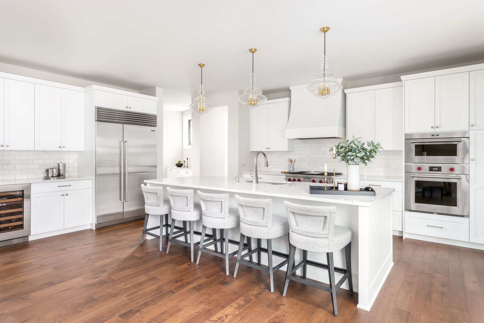Modern white kitchen with island, stainless steel appliances, and dark wood floors.