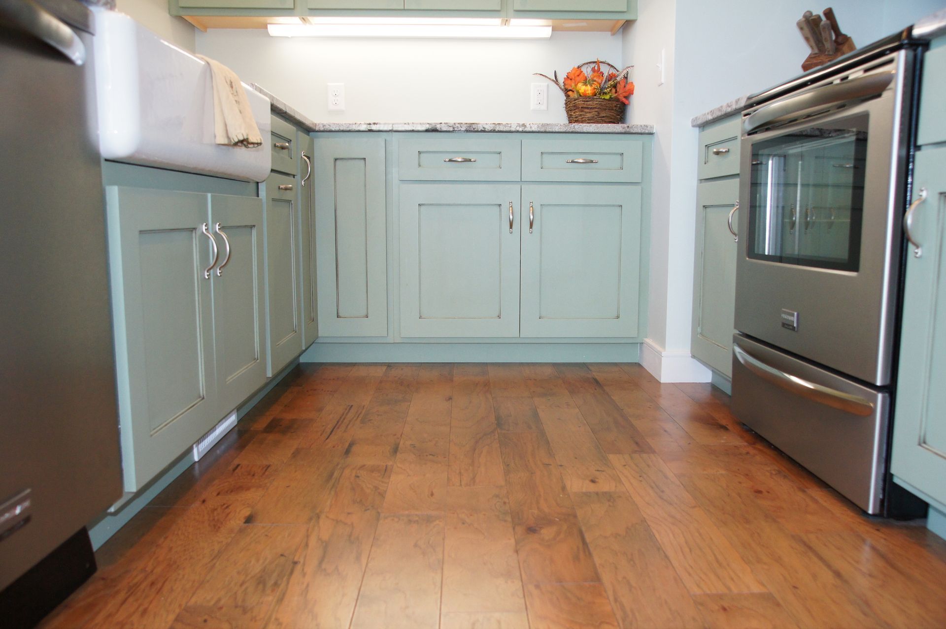 Kitchen with light blue cabinets, stainless steel appliances, and wood flooring.