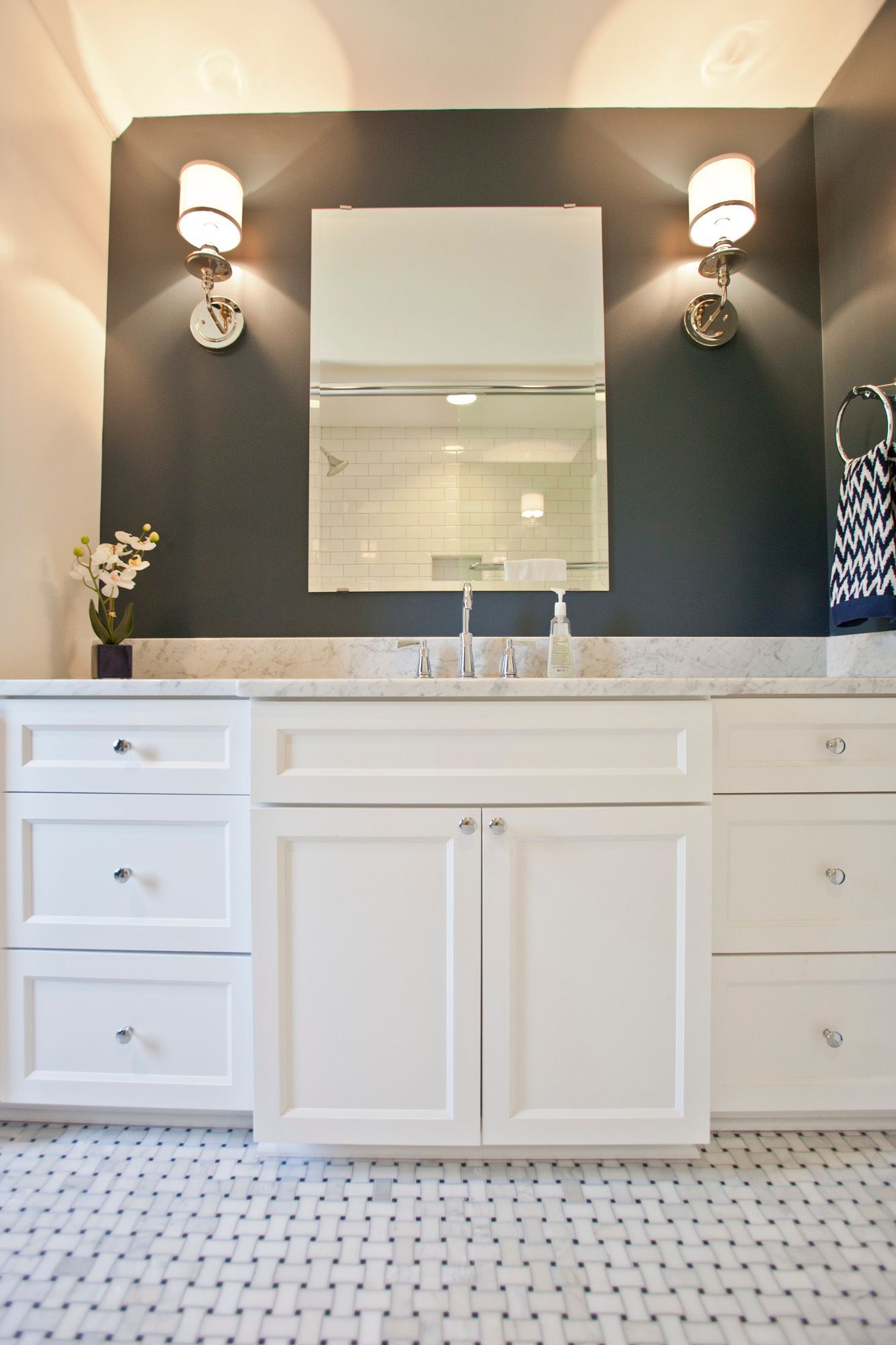 Bathroom with white vanity, dark gray wall, mirror, sconces, and mosaic floor.