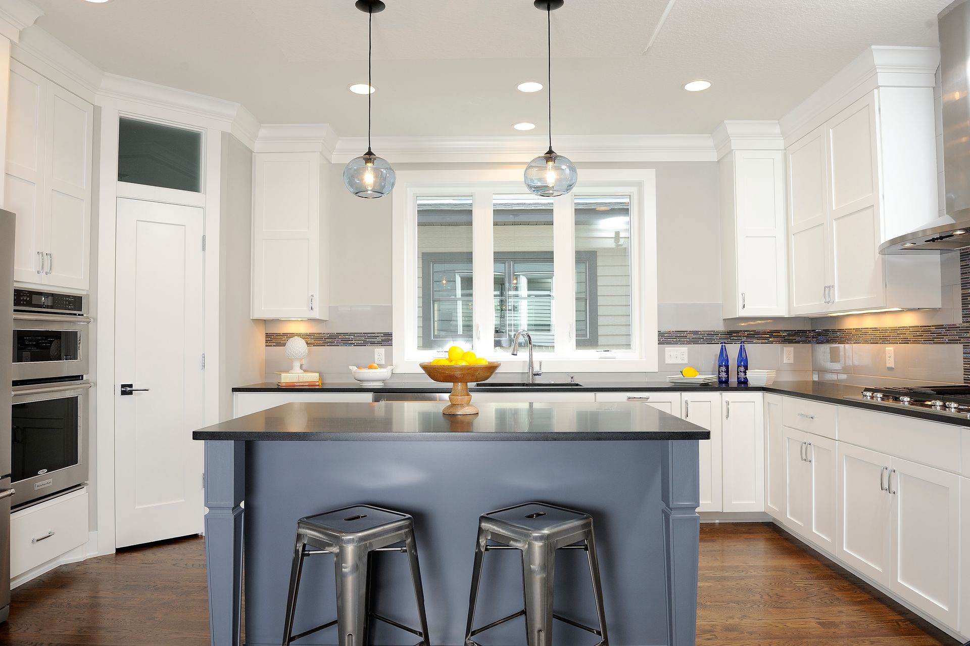Kitchen with white cabinets, blue island, two stools, and a window.