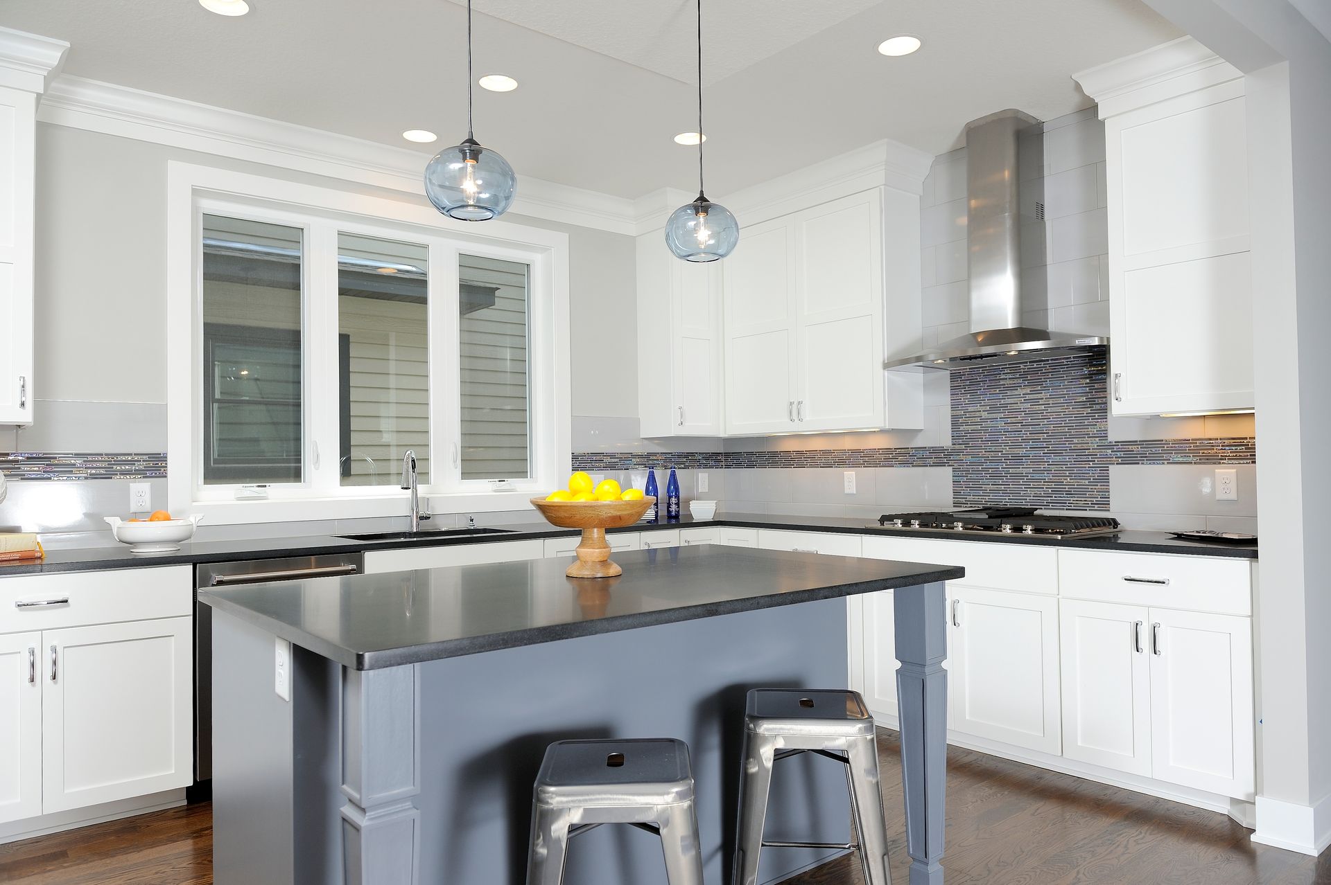 White kitchen with island, pendant lights, stainless steel appliances, and a window.