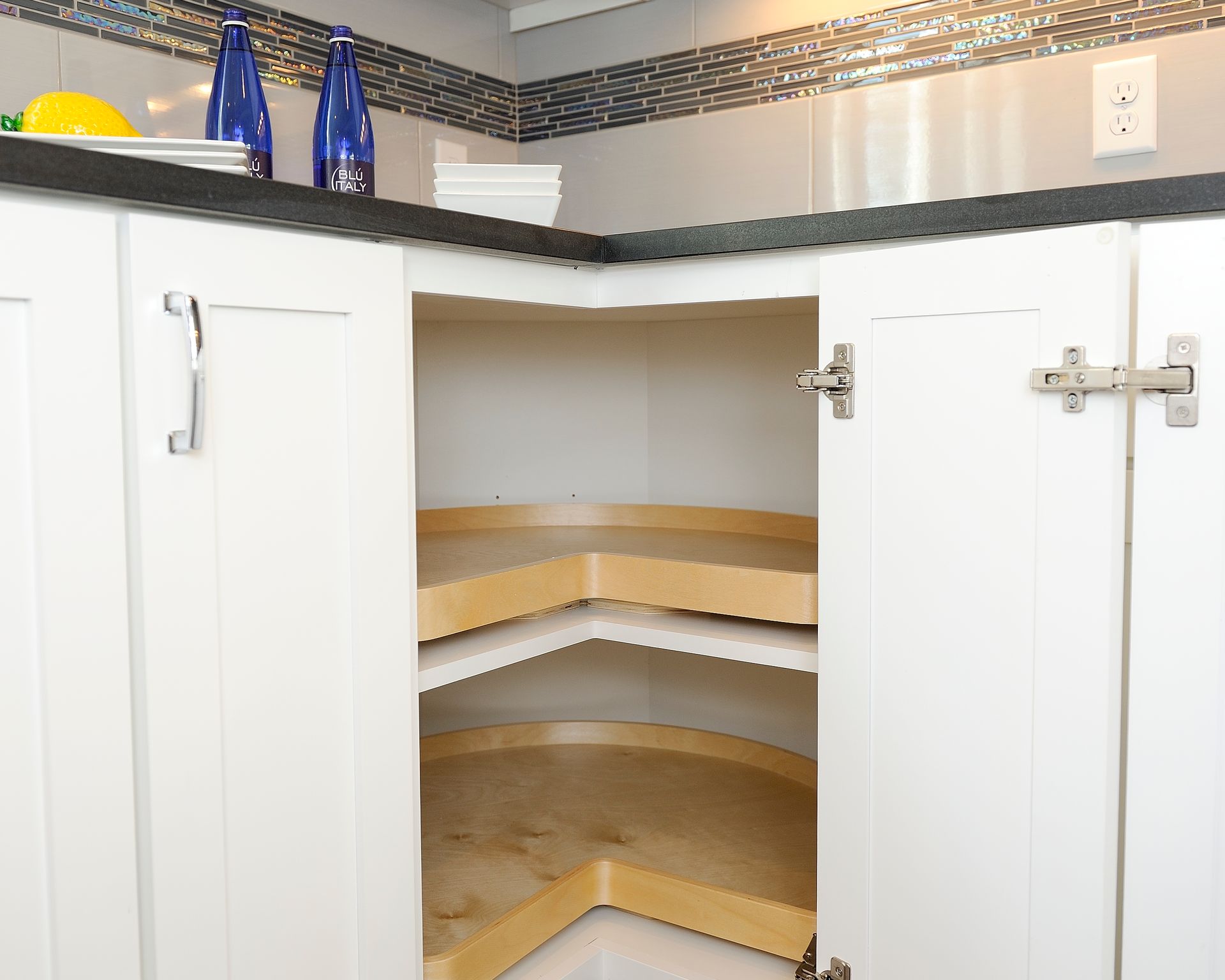 White corner kitchen cabinet with open doors, revealing two rotating shelves.