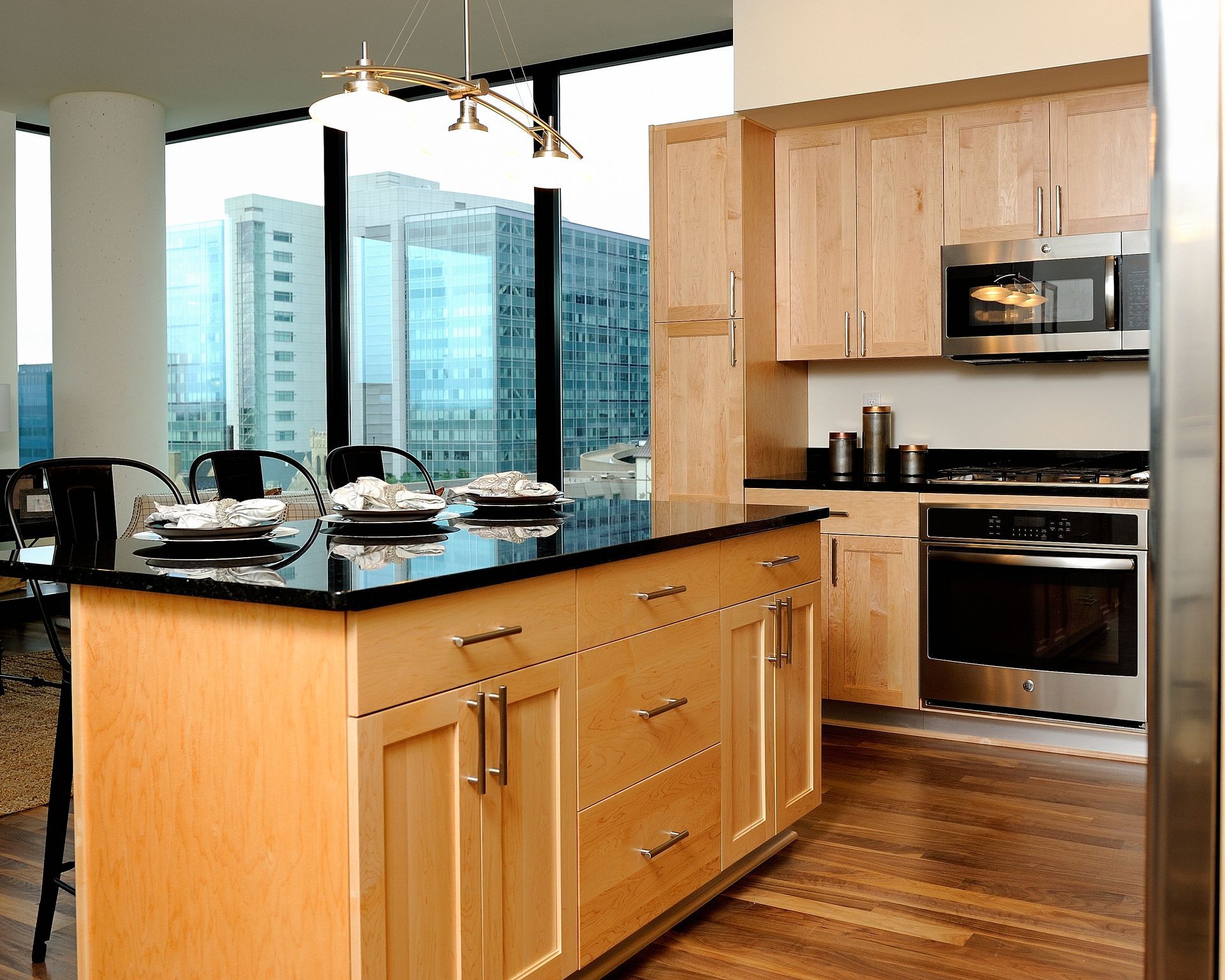 Modern kitchen with wood cabinets, black island countertop, stainless steel appliances, and city view.