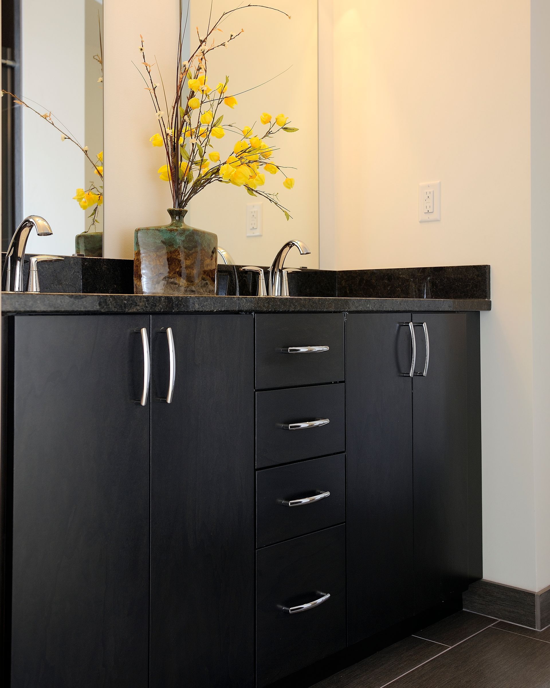 Black bathroom vanity with granite countertop, mirror, and yellow floral arrangement.