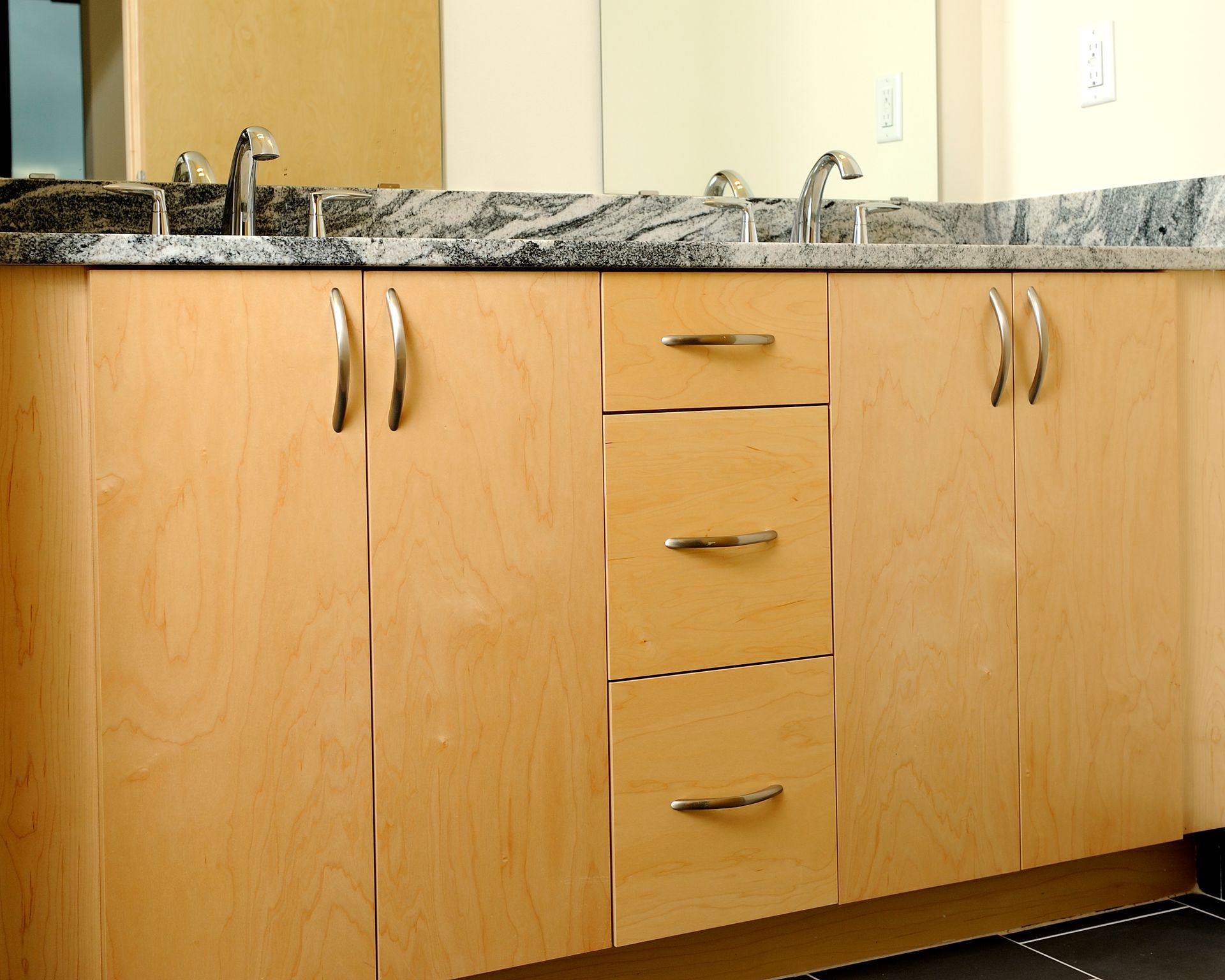 Bathroom vanity with light wood cabinets, granite countertop, and silver fixtures.