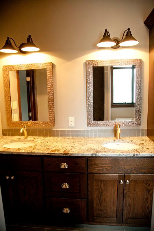Two vanity mirrors with bronze lighting above a double sink vanity with granite countertop.