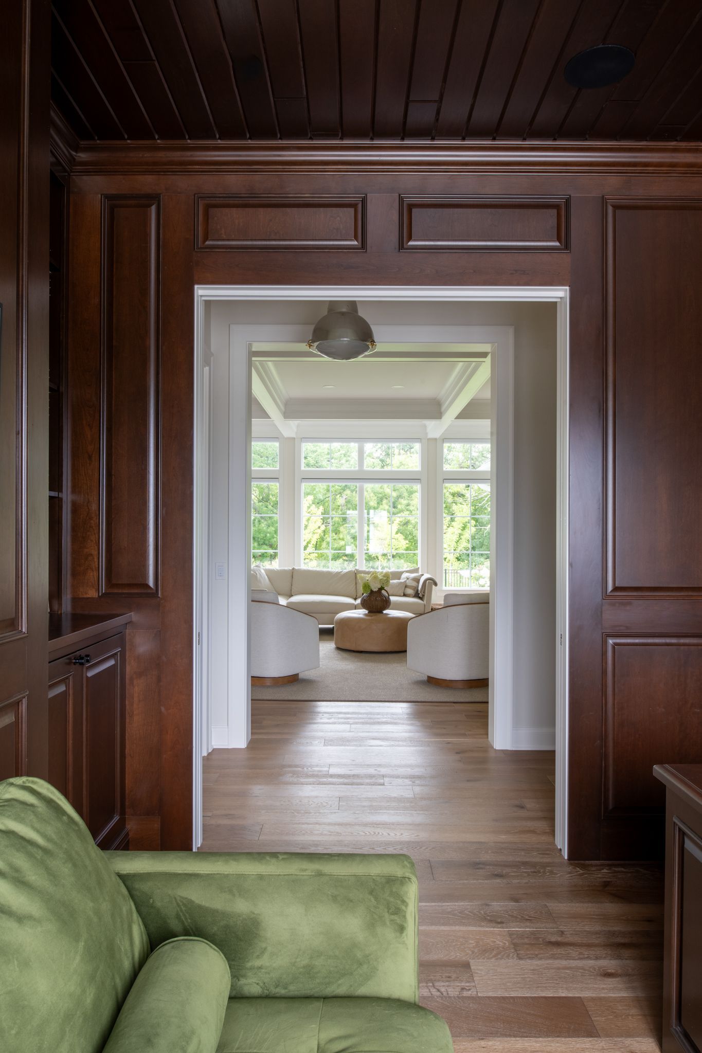 Dark wood-paneled doorway leading to a bright room with a sofa. A green couch is visible in the foreground.