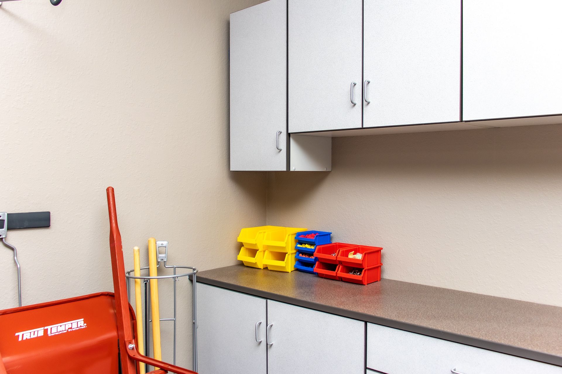 White cabinets in a room with a red cart, a gray wire rack with tools, and colorful bins on a countertop.