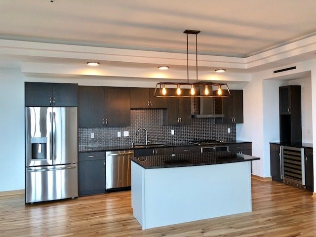 Modern kitchen with dark cabinetry, stainless steel appliances, and a black countertop island.