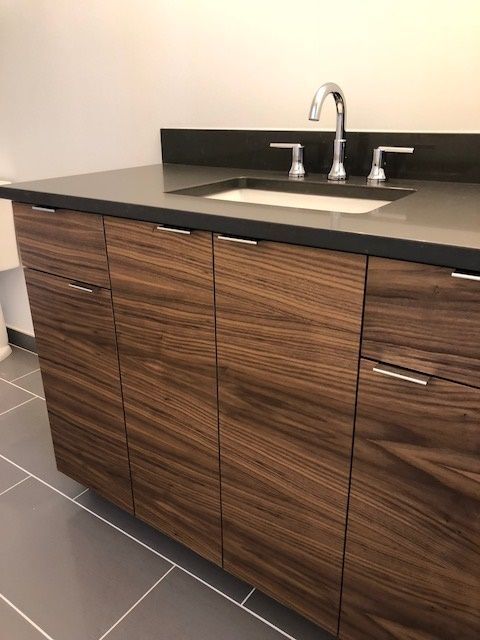Dark wood bathroom vanity with a dark countertop and silver faucet.