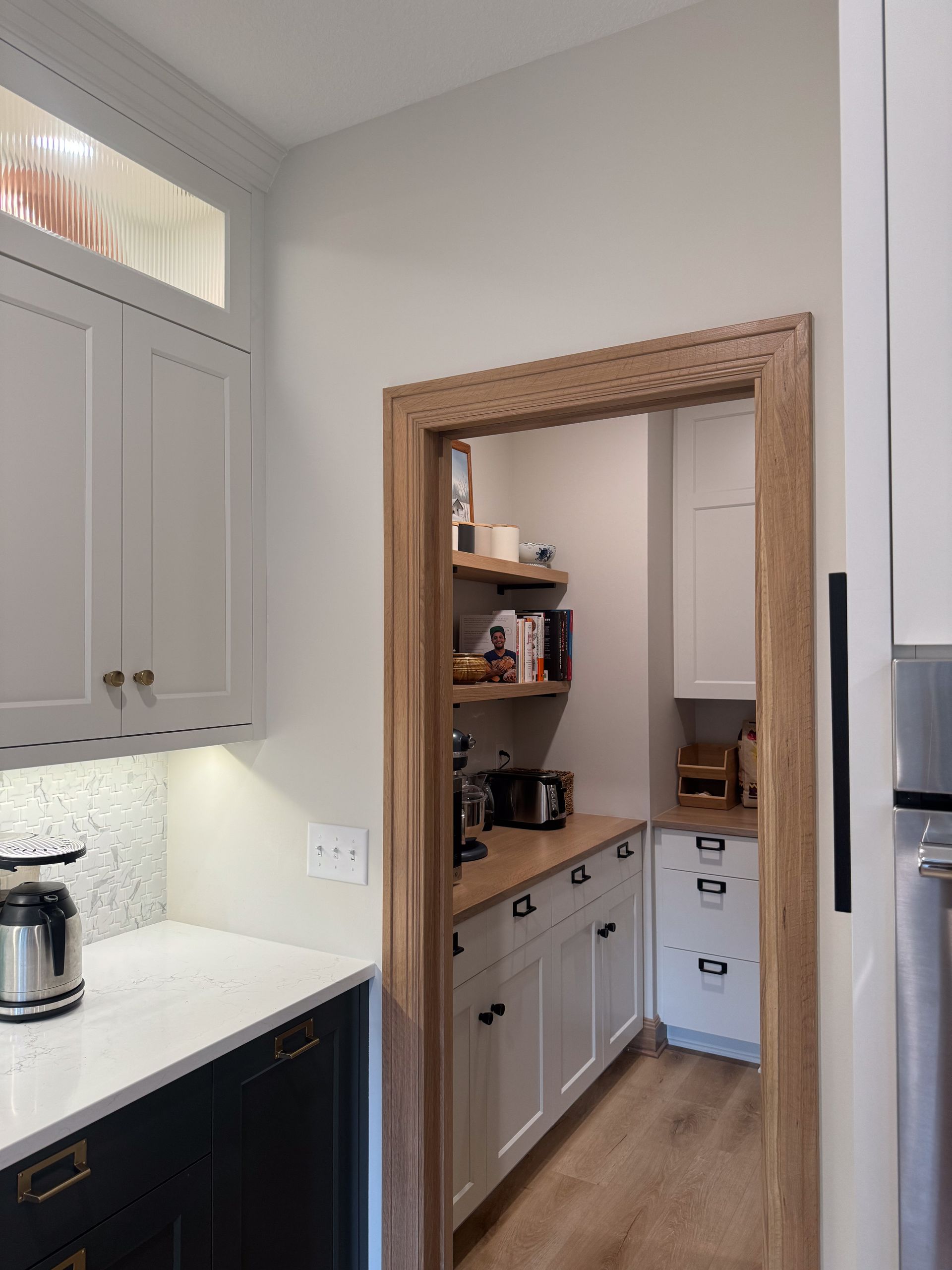 Kitchen with pantry entrance, light wood trim, white and black cabinets, and wooden shelves.