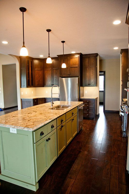 Kitchen with green island, granite countertop, dark wood cabinets, pendant lights.