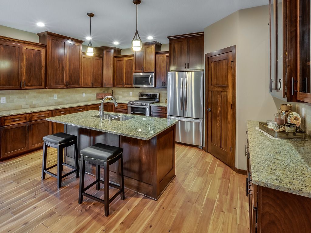 A kitchen with dark wood cabinets, a granite countertop island, and stainless steel appliances.