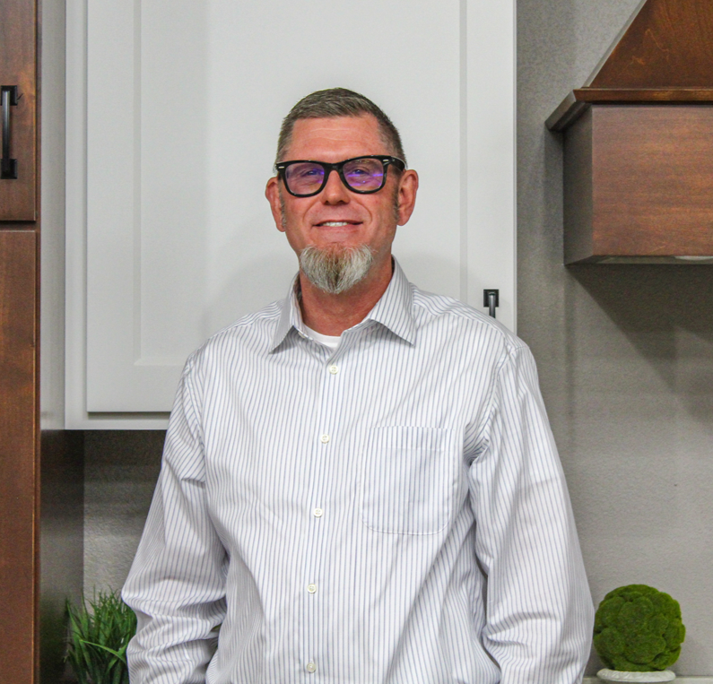Man with glasses and goatee in a striped shirt, standing in front of white cabinets.