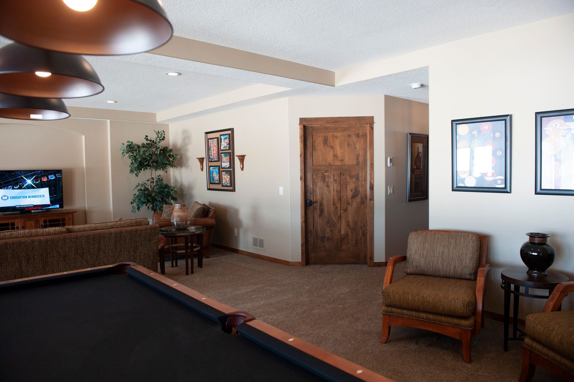 A rec room with a pool table, seating area, TV, and wooden door.