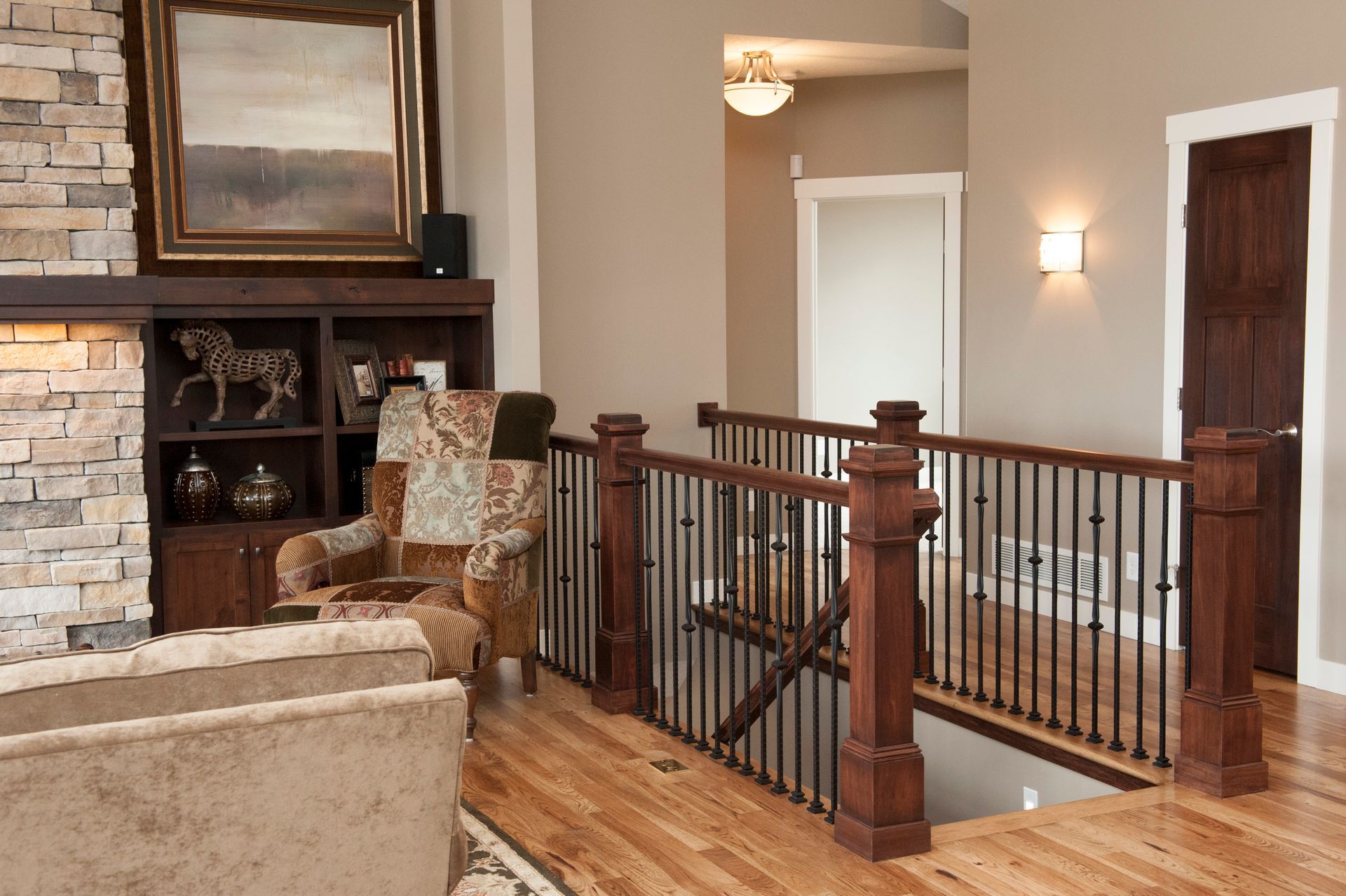 Interior view of a hallway with a wooden railing, stone fireplace, and a sitting area with a patterned armchair.