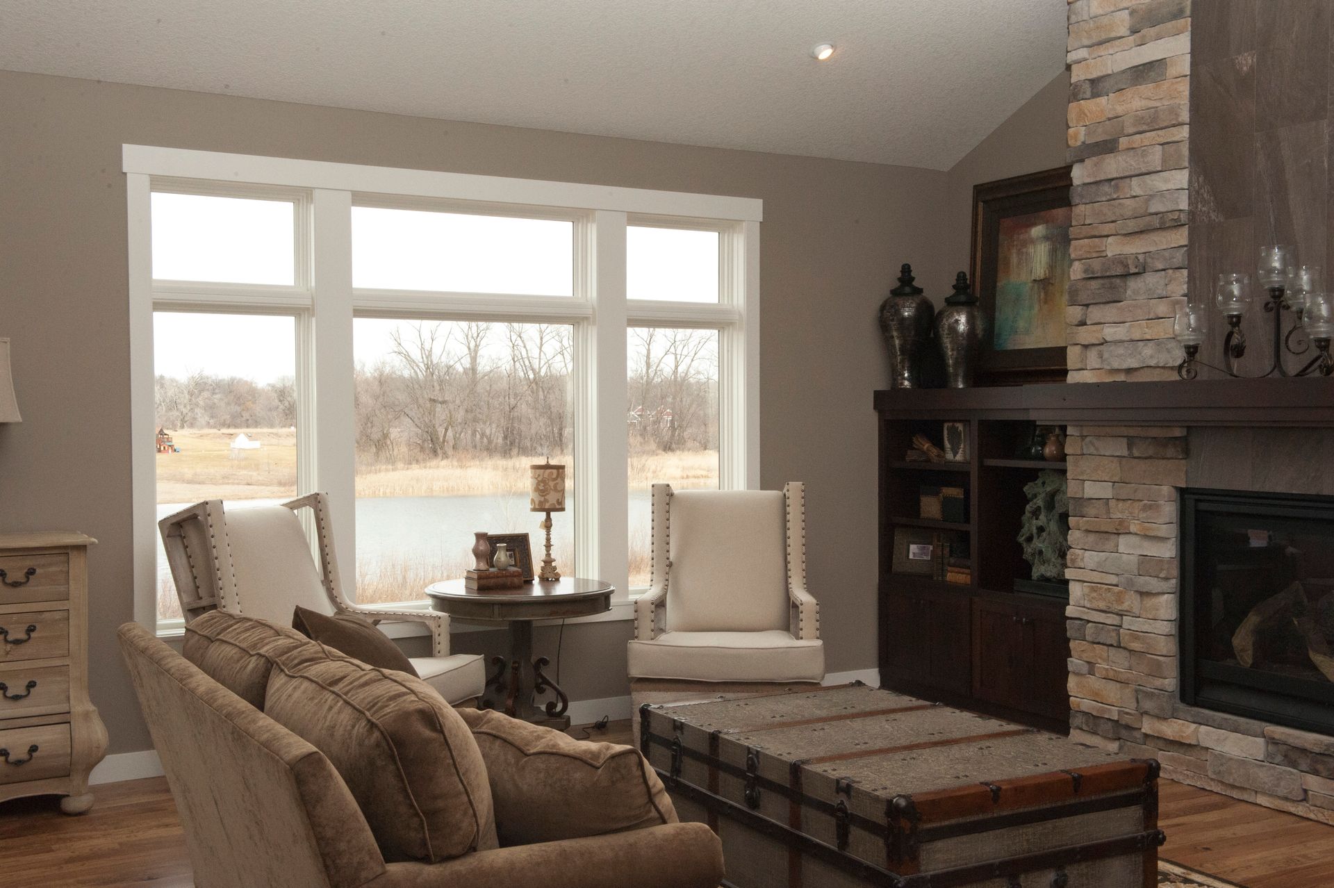 Living room with stone fireplace, large window overlooking a pond, sofa, and chairs.