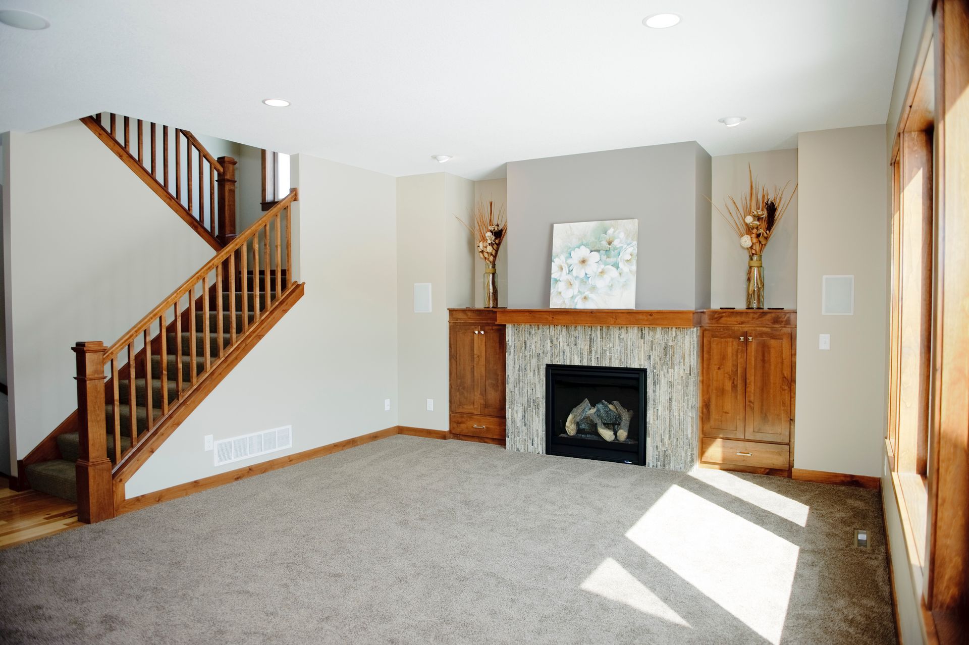 Empty living room with fireplace, staircase, and carpet. Light brown wood accents and neutral walls.