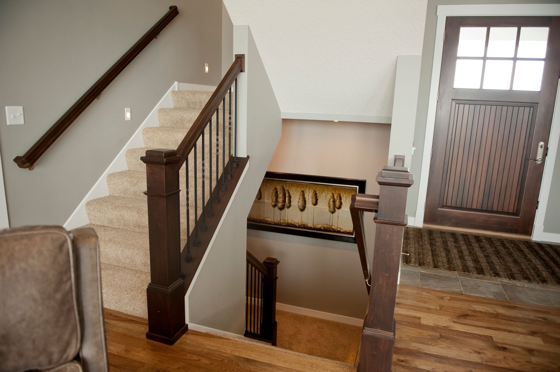 Staircase with carpeted steps, dark wooden railing, and a front door. Gray walls and wood flooring are present.