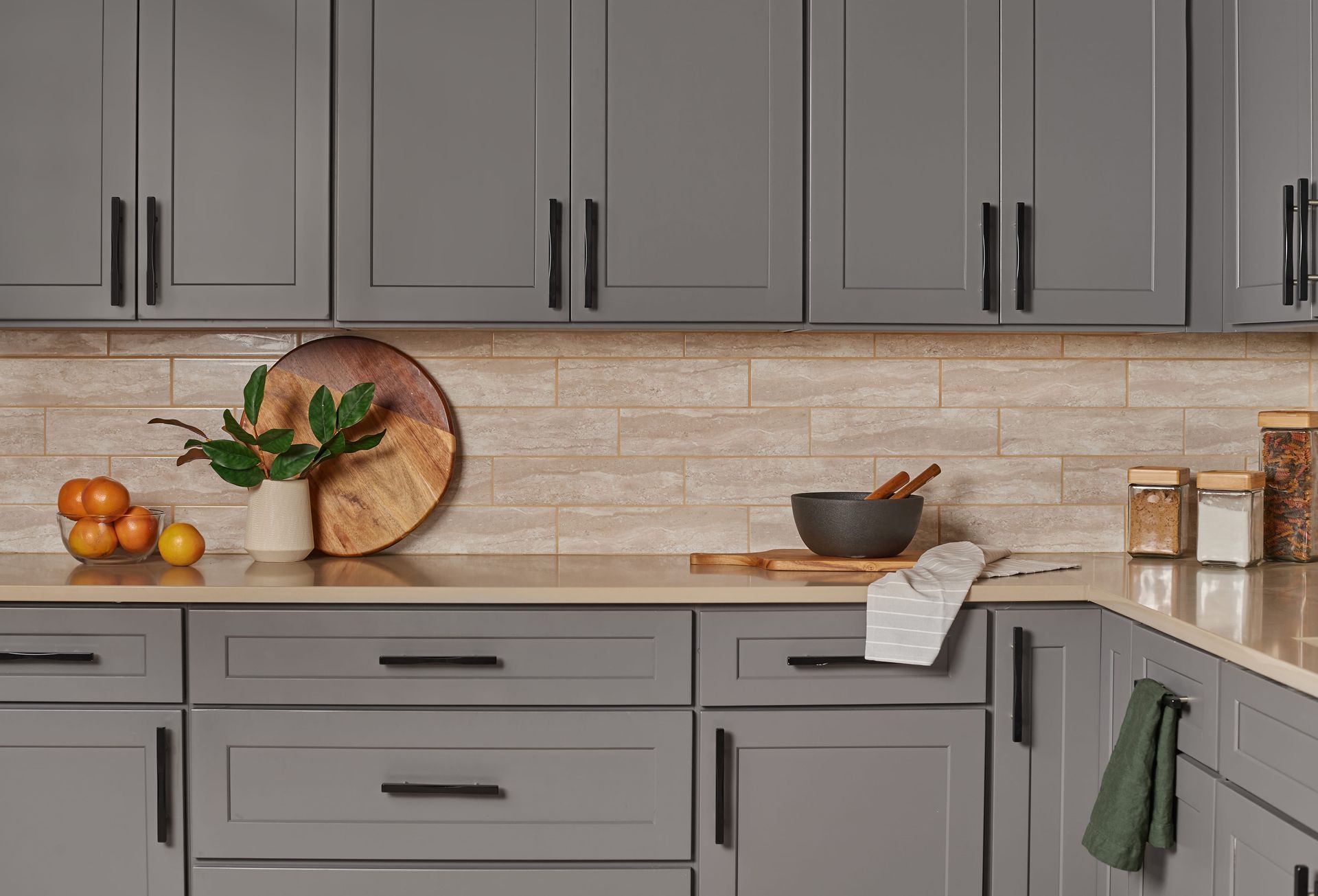 Gray kitchen cabinets with black handles, light countertops, and wooden backsplash.