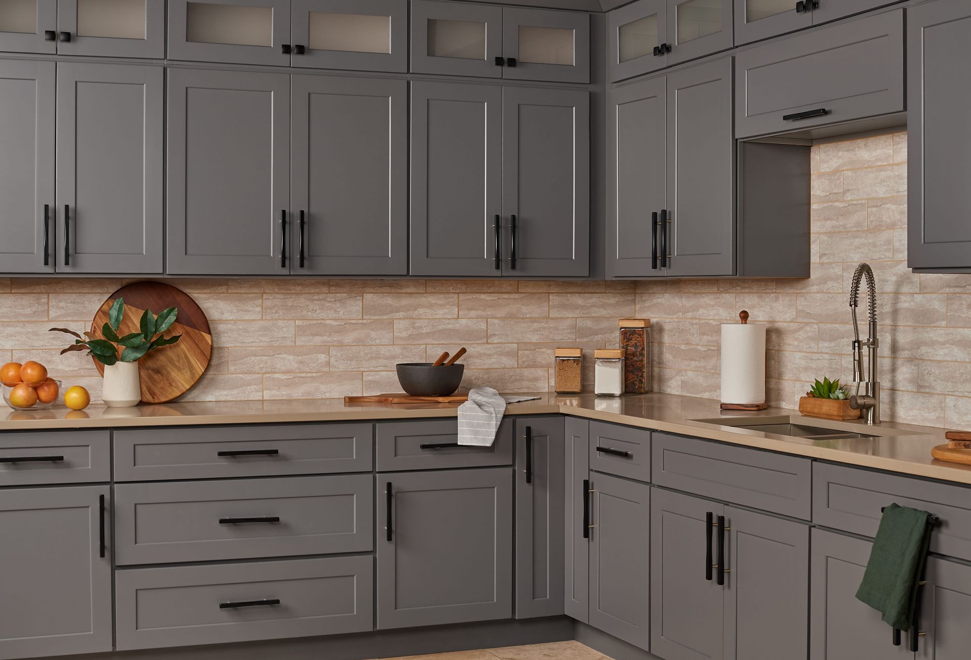 Gray kitchen cabinets with black hardware and light-colored backsplash.