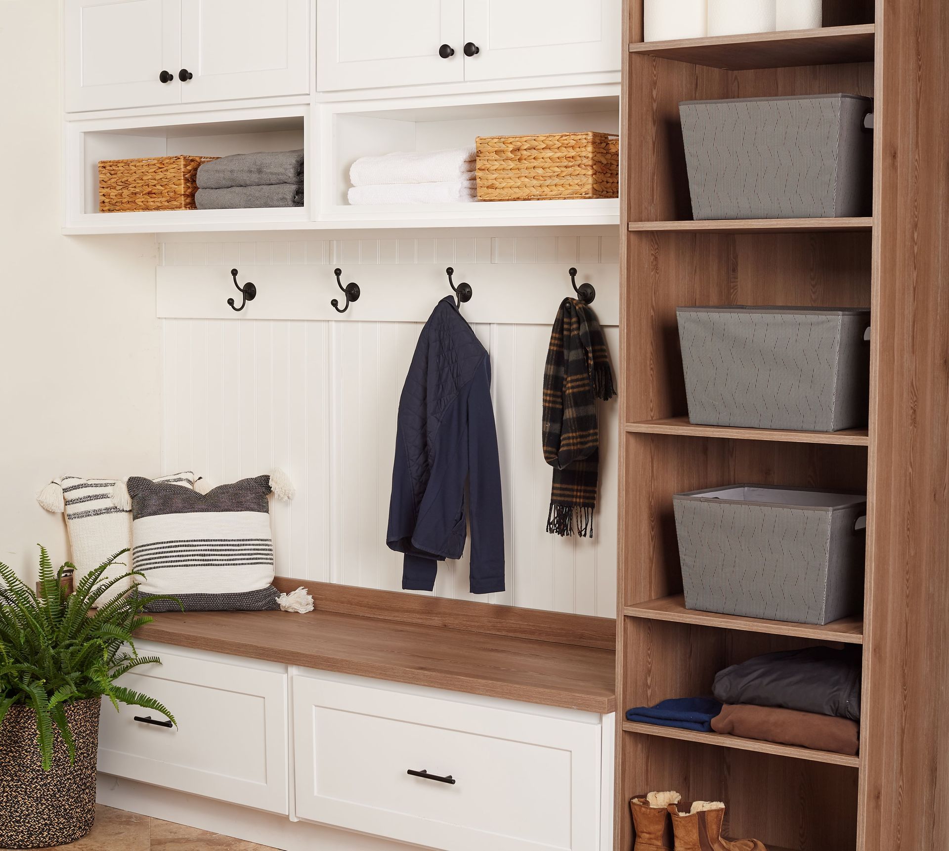 Mudroom with storage: white cabinets, bench, hooks, brown shelving with bins and folded clothes.
