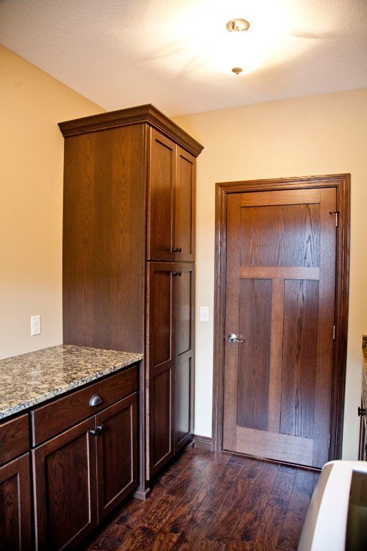 Dark wood pantry cabinet and cabinets with granite countertop in a kitchen; doorway on the right.