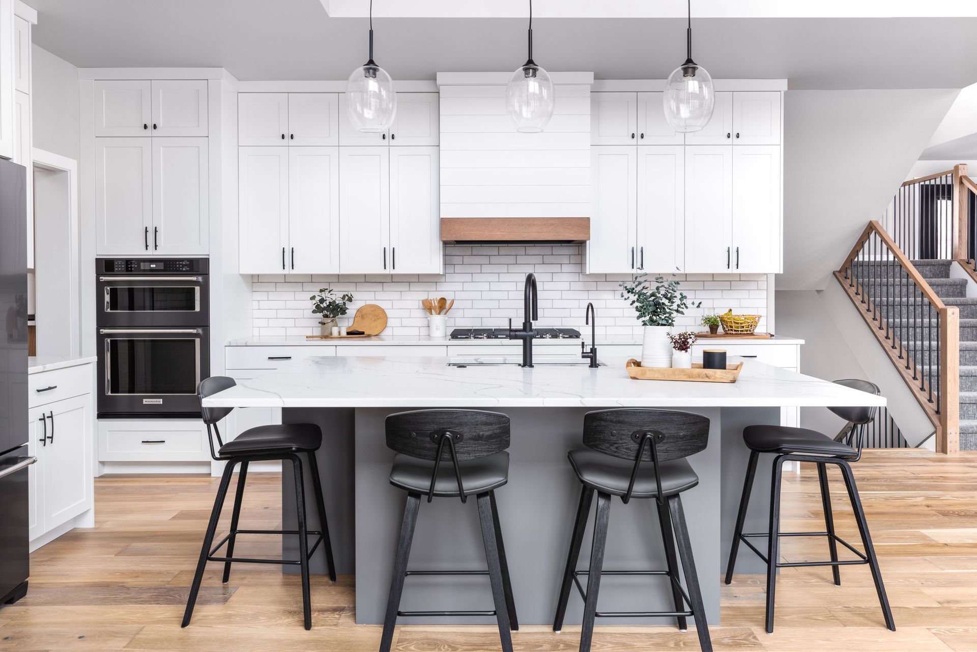 Modern white kitchen with gray island, black stools, and pendant lights.