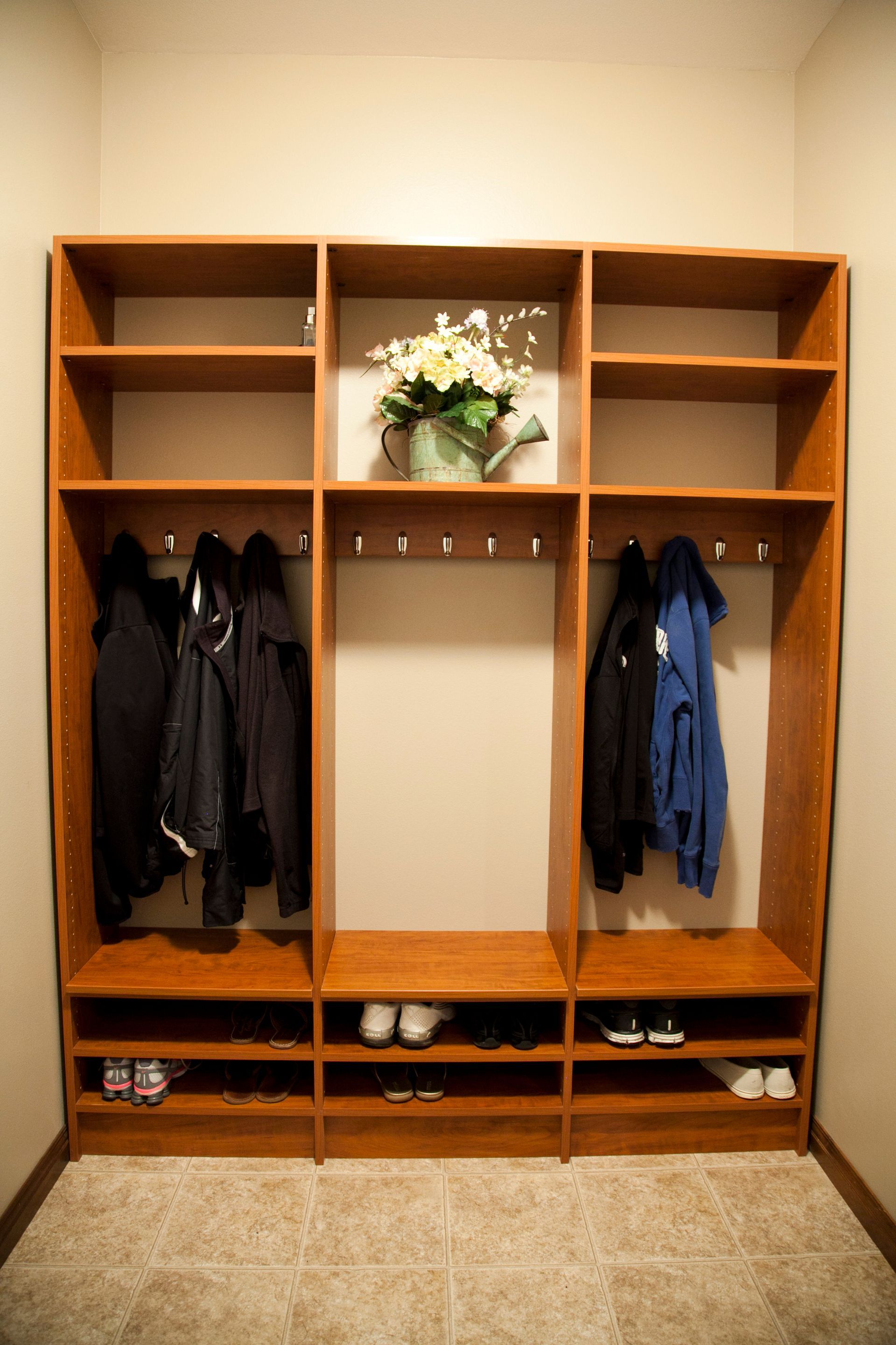 Wooden entryway storage unit with shelves, hooks, and shoe cubbies. Coats hang inside.