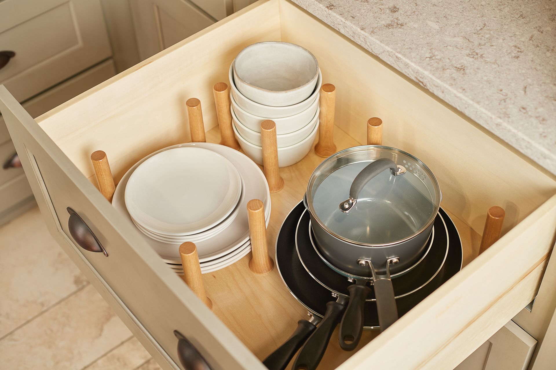 Drawer with wooden dividers organizing dishes and cookware in a kitchen cabinet.
