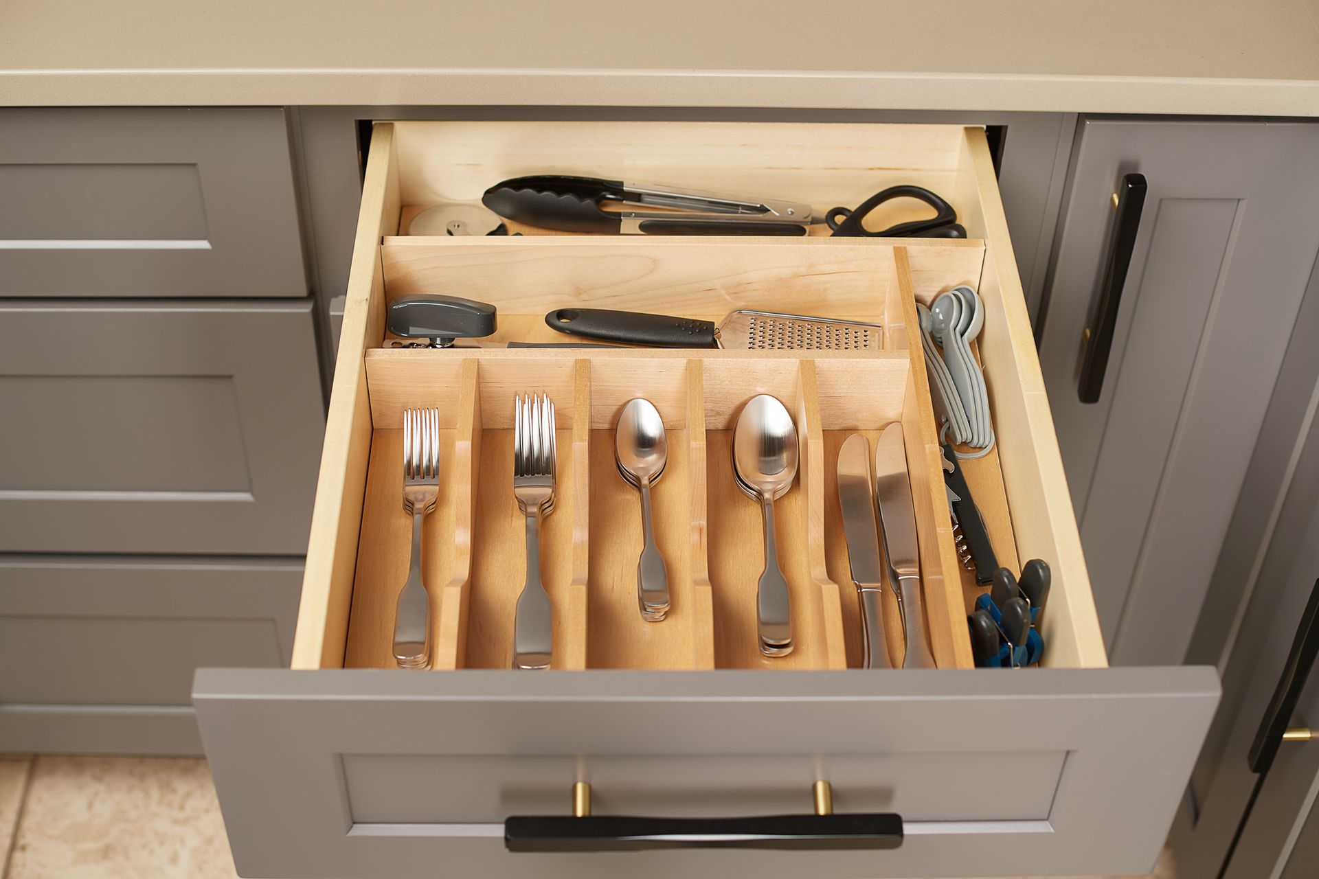Open kitchen drawer with wooden utensil organizer holding silverware and cooking tools.