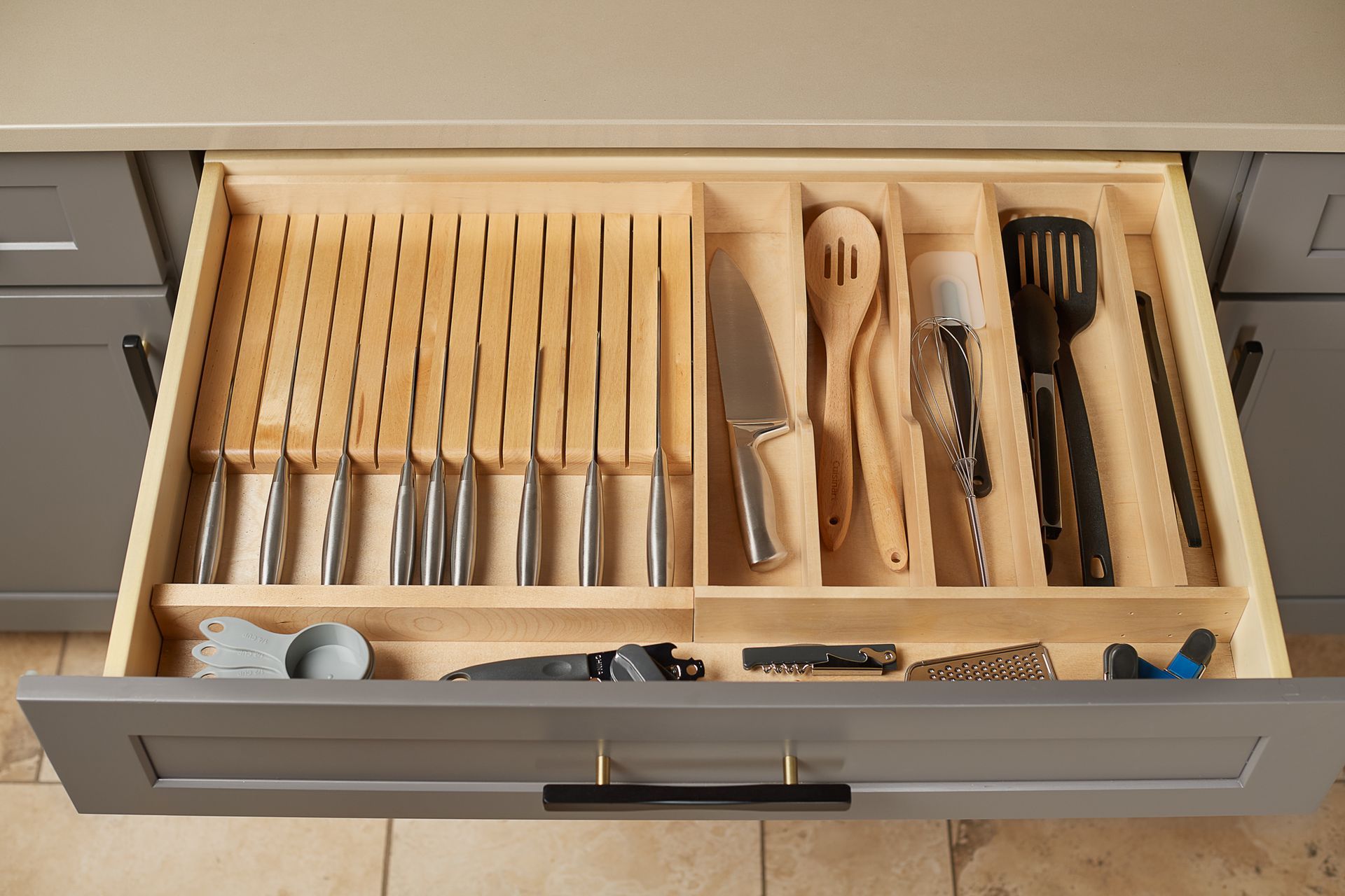 Open kitchen drawer with wooden knife block, utensils. Silver knives, wooden spoons, black spatula.