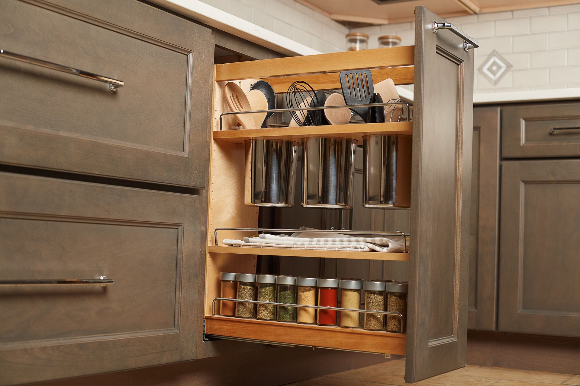 Gray kitchen cabinet with pull-out spice rack and storage for utensils. A cat is in the center.