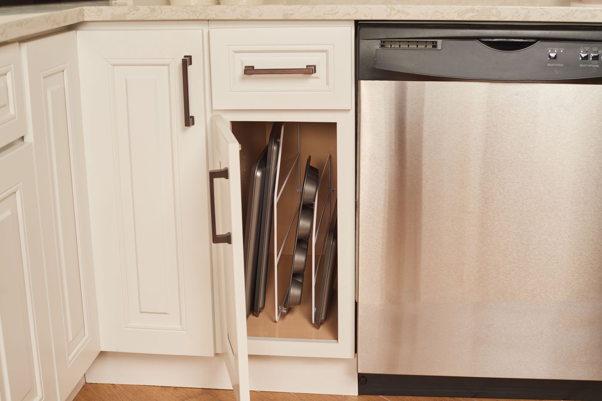 White kitchen cabinet with vertical storage for baking sheets next to a stainless steel dishwasher.
