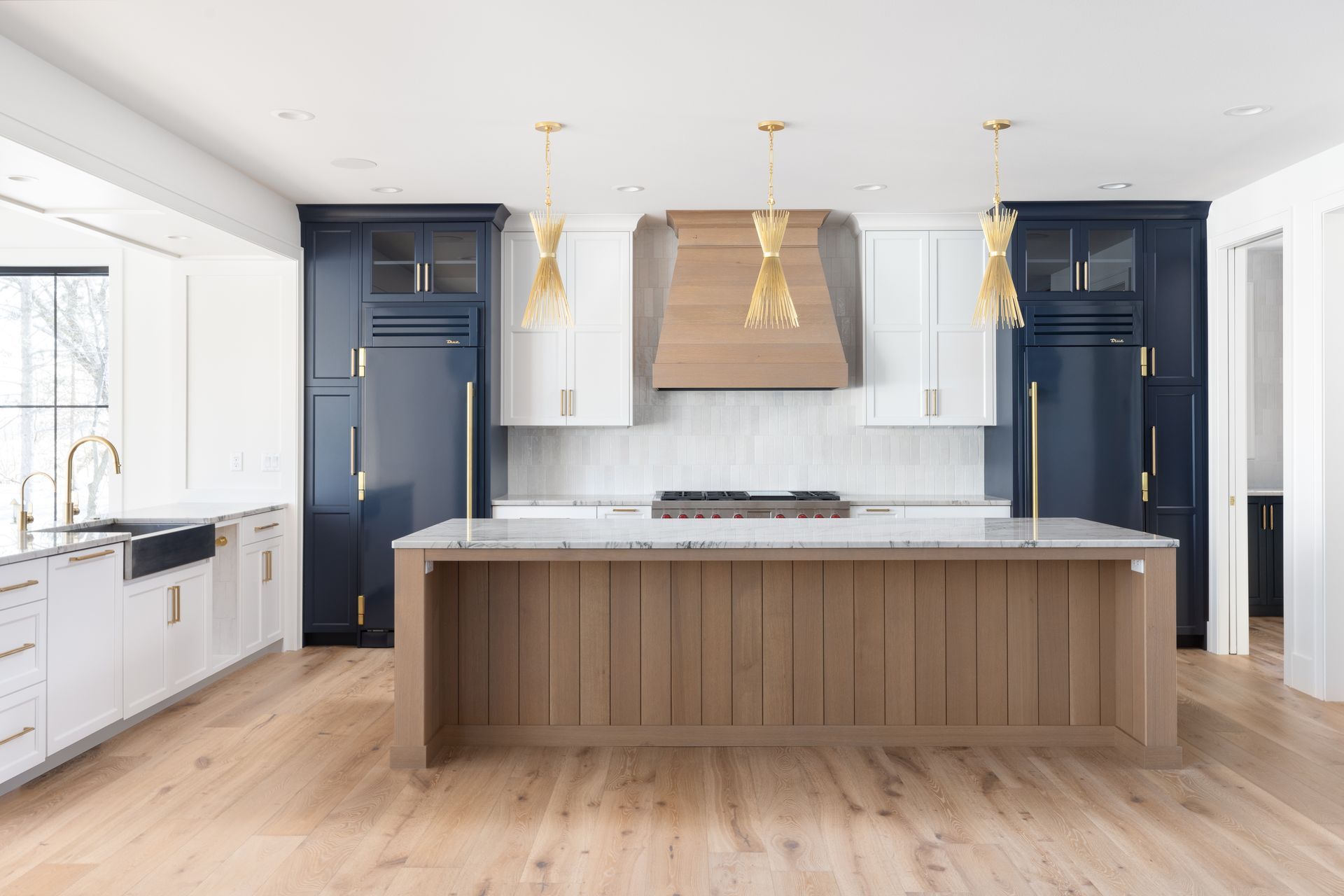 Modern kitchen with blue and white cabinets, wood island and hood, gold accents, and hardwood floors.