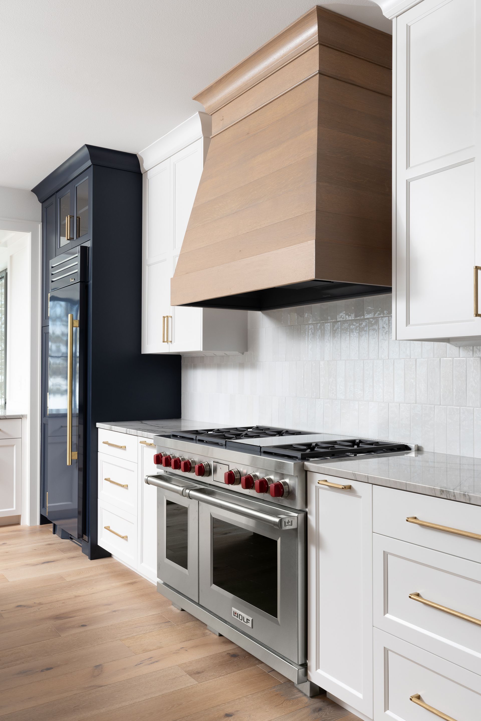 Modern kitchen with white cabinets, stainless steel oven, and wooden range hood.