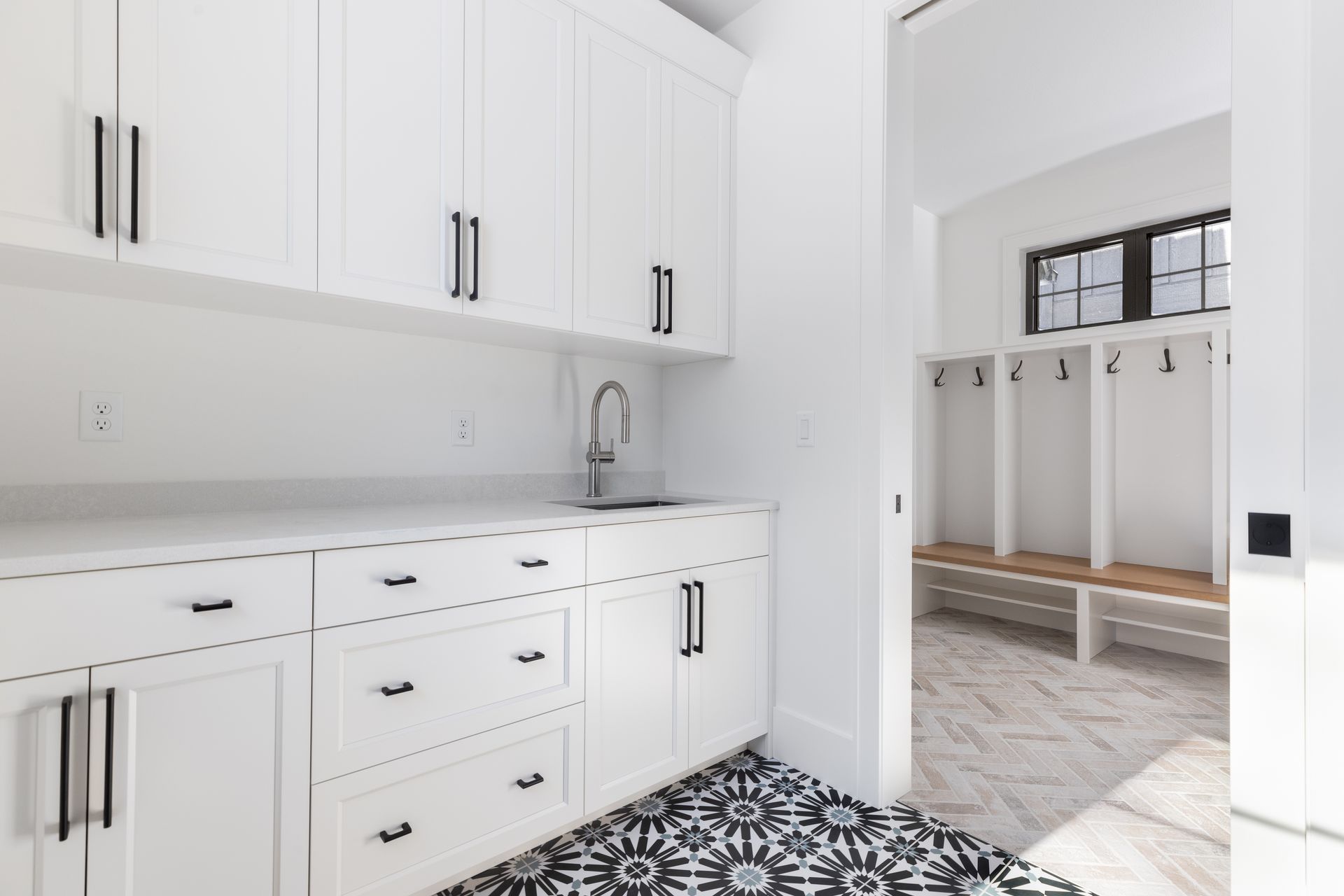 White laundry room with black hardware and patterned floor, leading to a hallway with lockers.