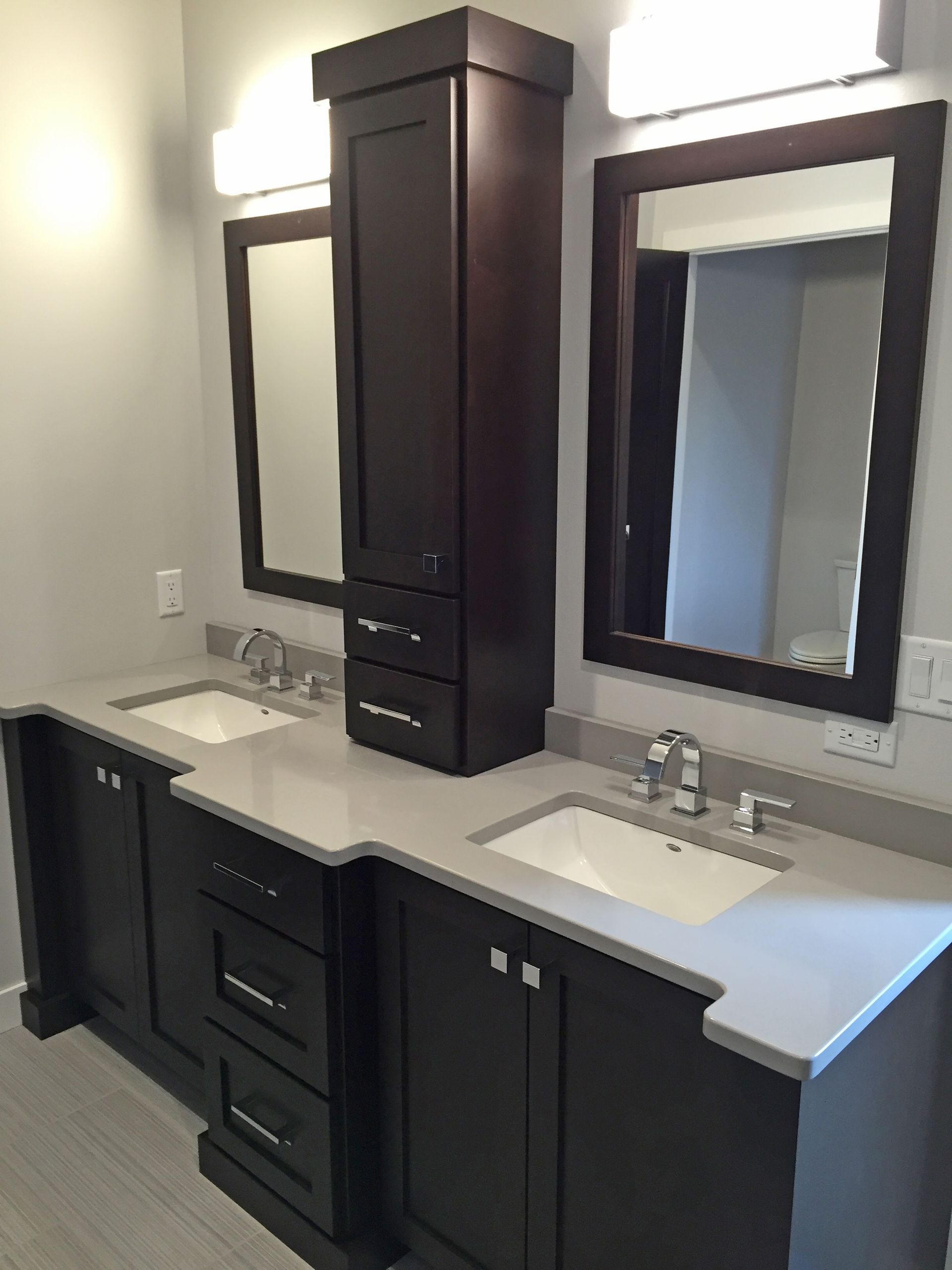 Dark wood double bathroom vanity with gray countertop, mirrors, and a tall cabinet.