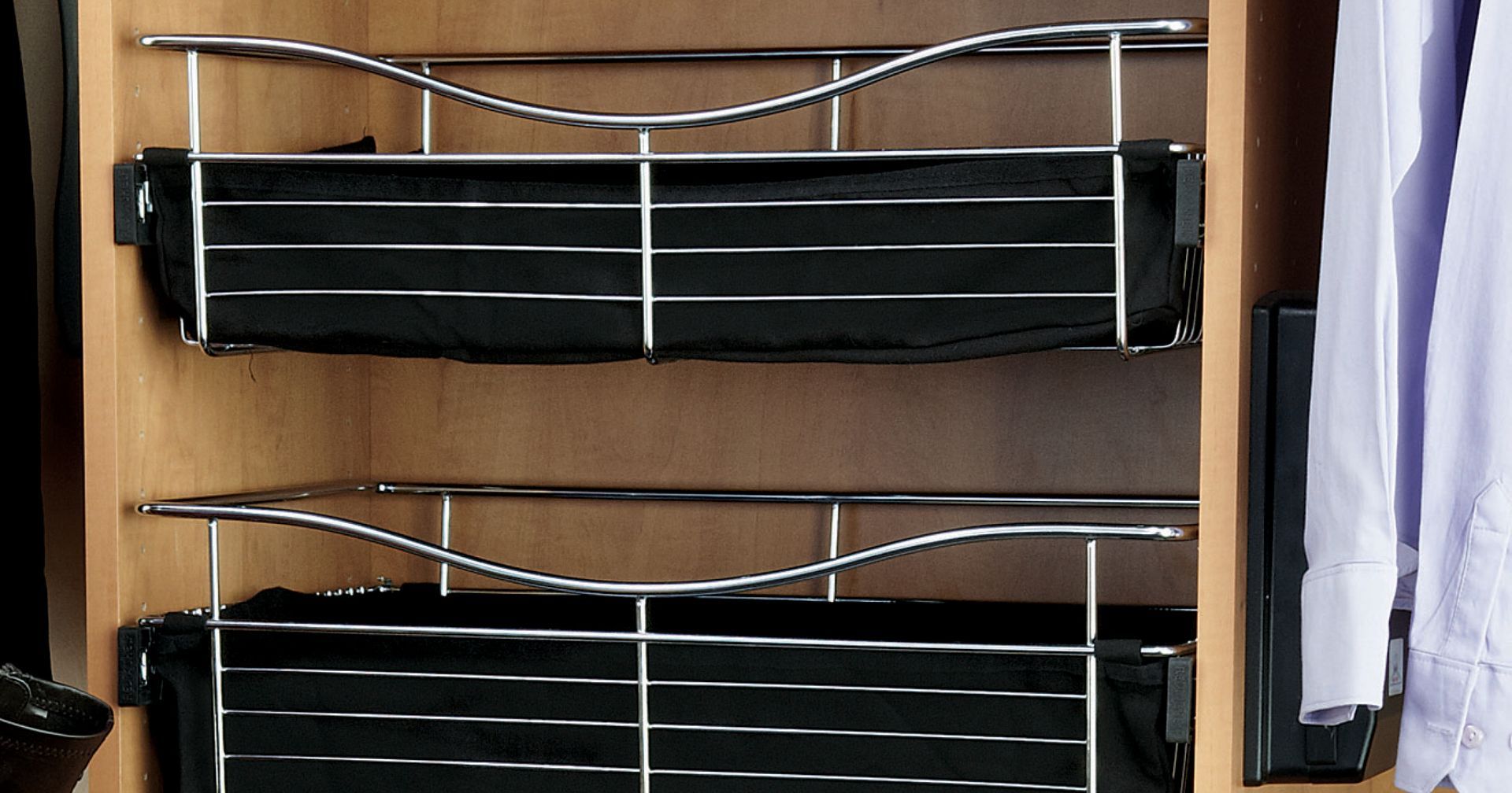Two black pull-out wire baskets in a wooden closet, with clothes on the right.