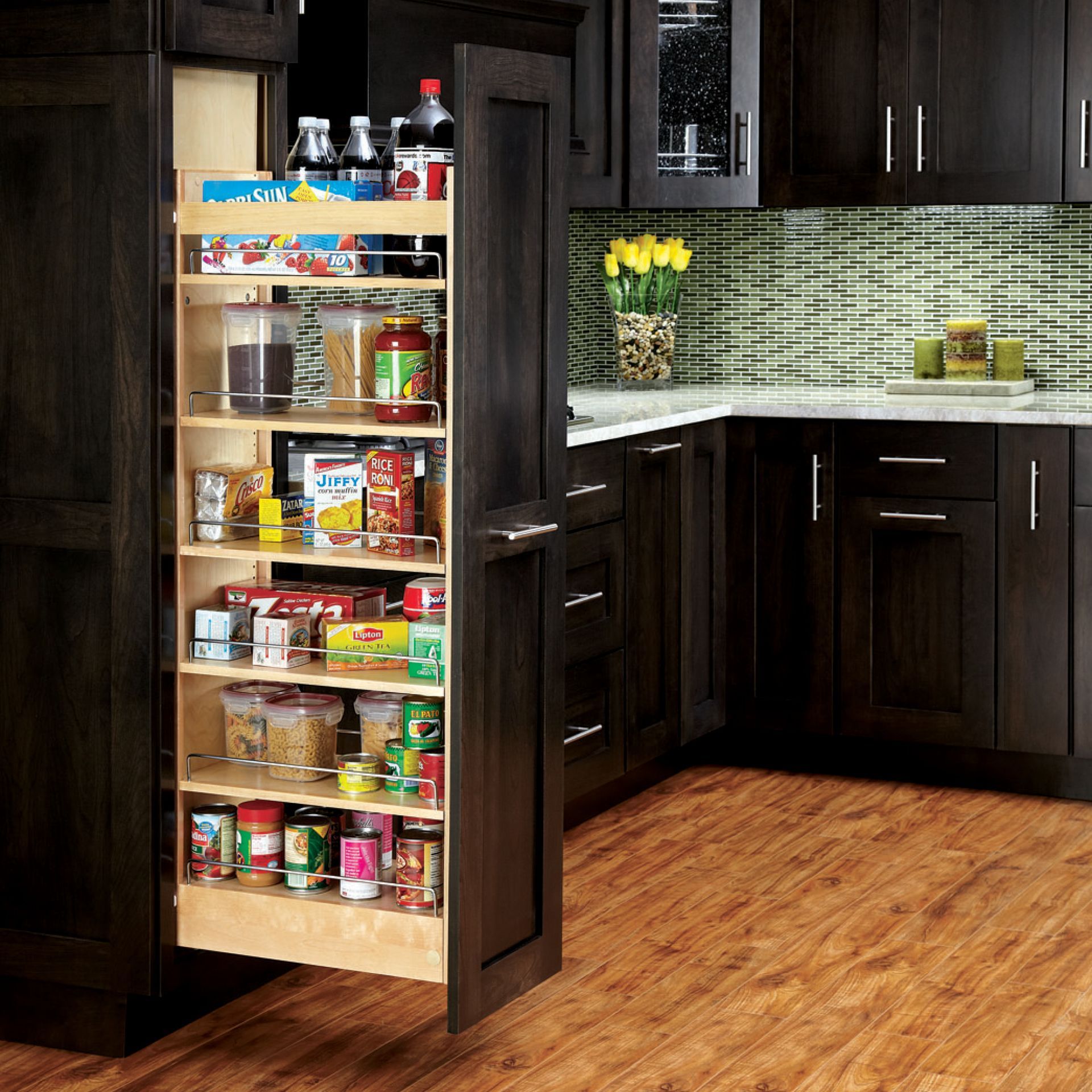 Pull-out pantry in dark kitchen; shelves filled with food items. Light wood flooring and green backsplash.