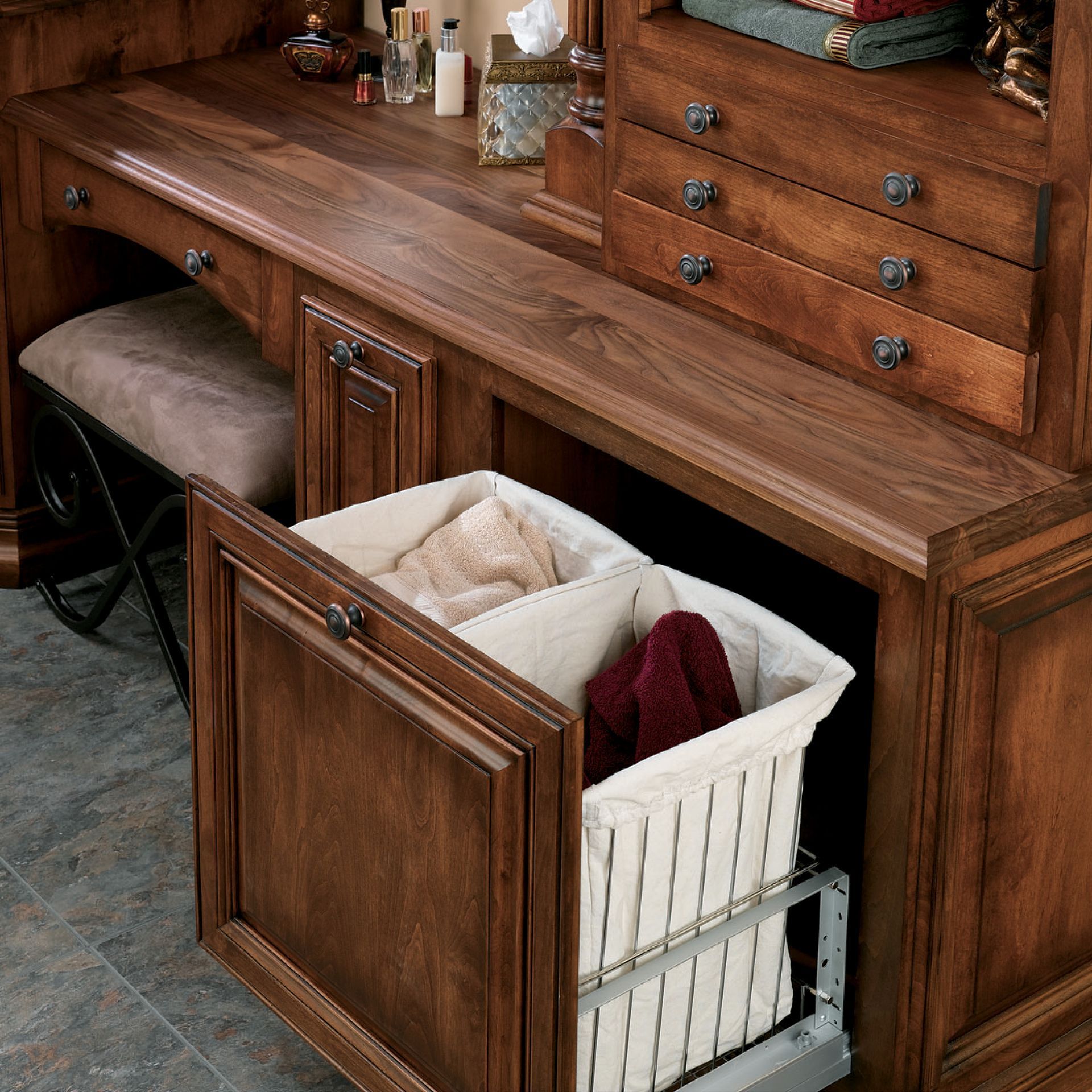 Wooden vanity with open cabinet revealing a pull-out laundry hamper with two compartments filled with clothing.