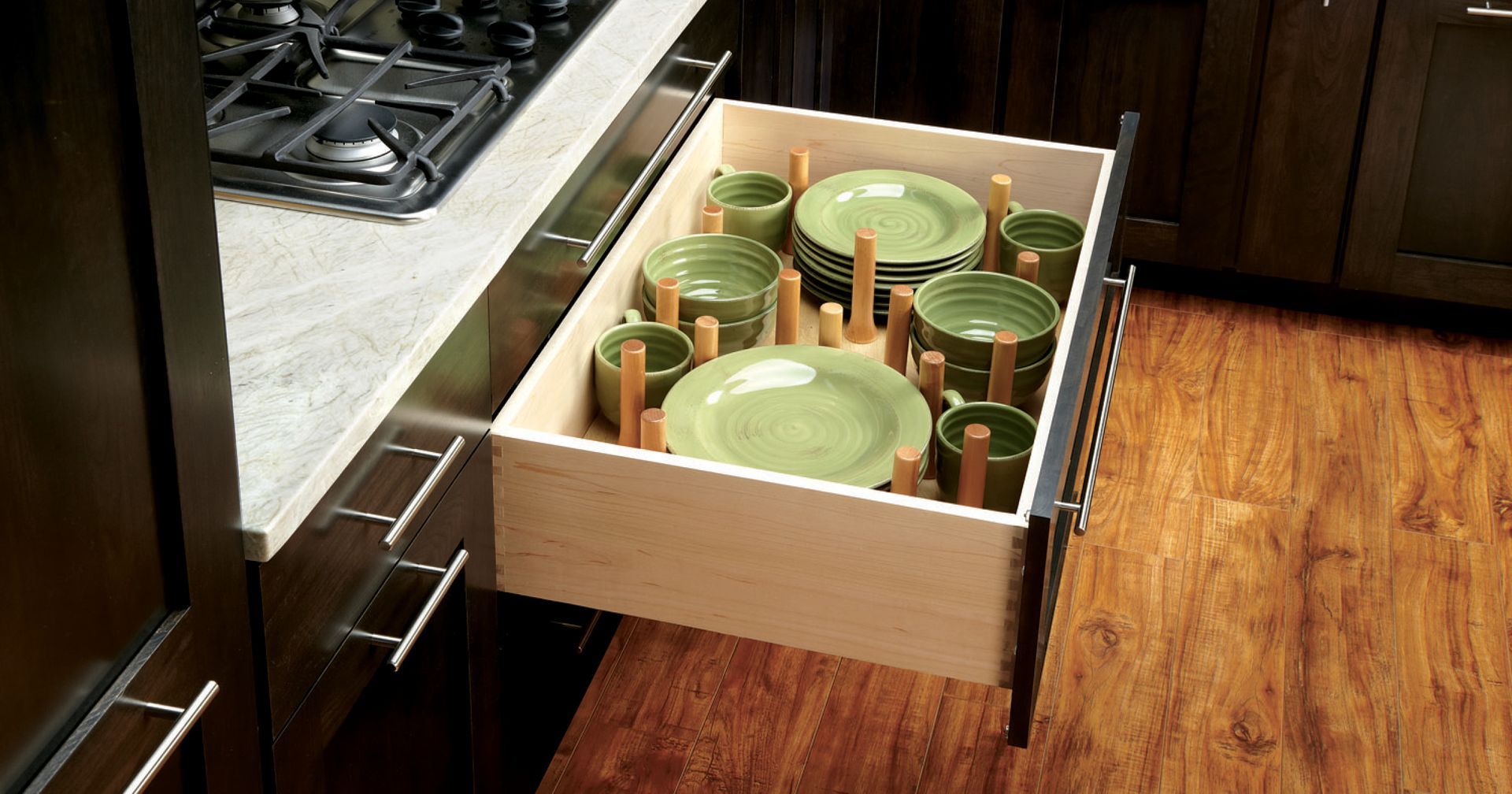 Open kitchen drawer holding stacked green plates, separated by wooden pegs.