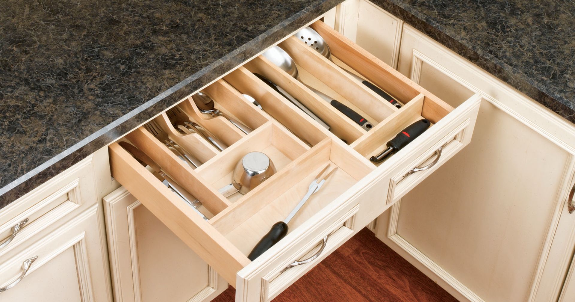 Opened kitchen drawer with silverware organizer, brown countertop, beige cabinets.