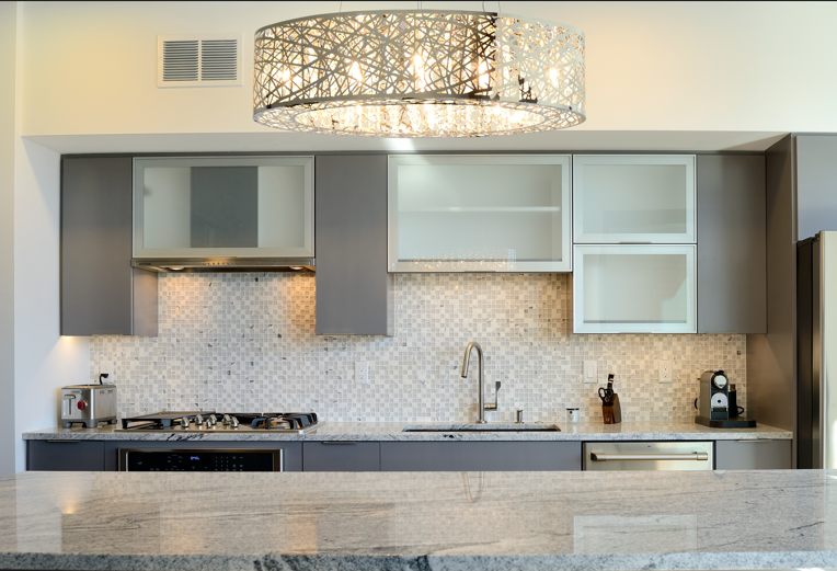 Modern kitchen with gray cabinets, mosaic backsplash, and decorative light fixture.