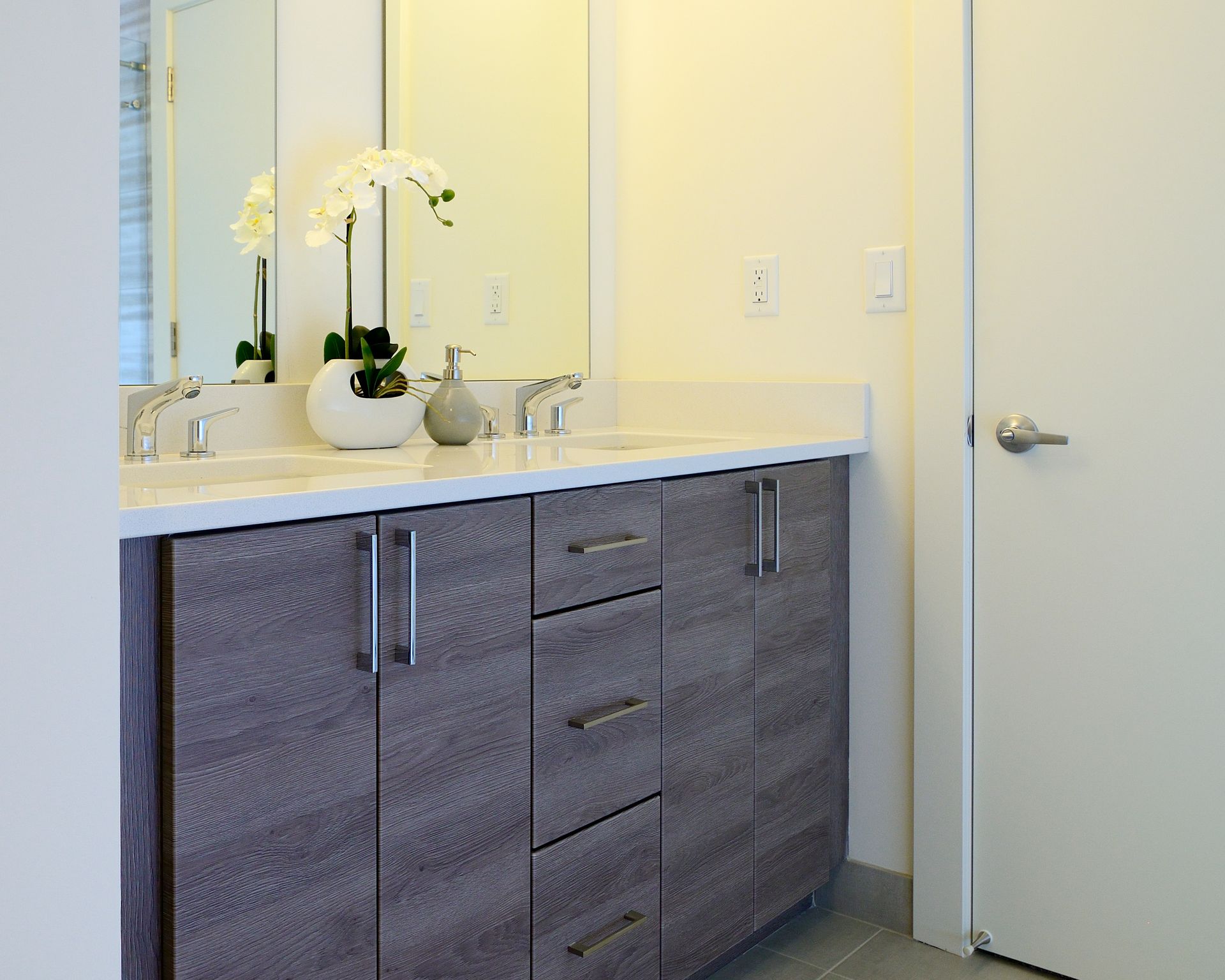 Bathroom with gray textured vanity, white countertop, double sinks, large mirror, and a white door.