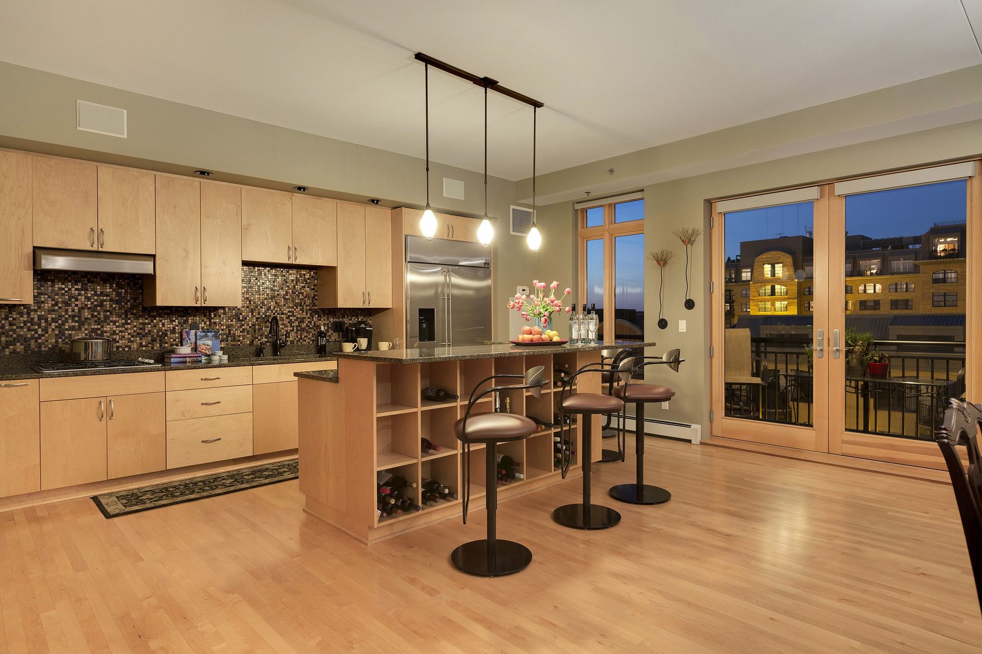 Modern kitchen with light wood cabinets, island with bar seating, and outdoor view.